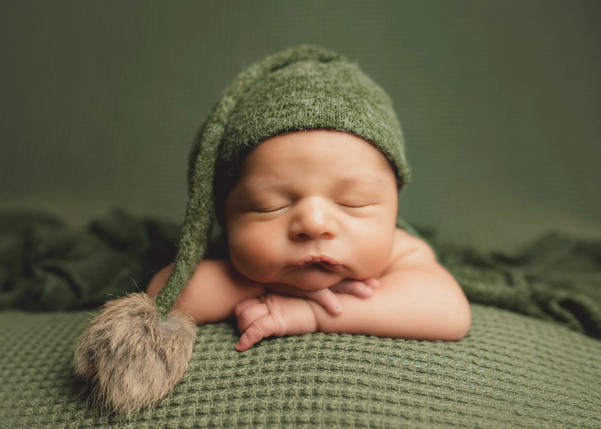 Sleeping newborn baby in a green knit hat during a posed newborn photography session.