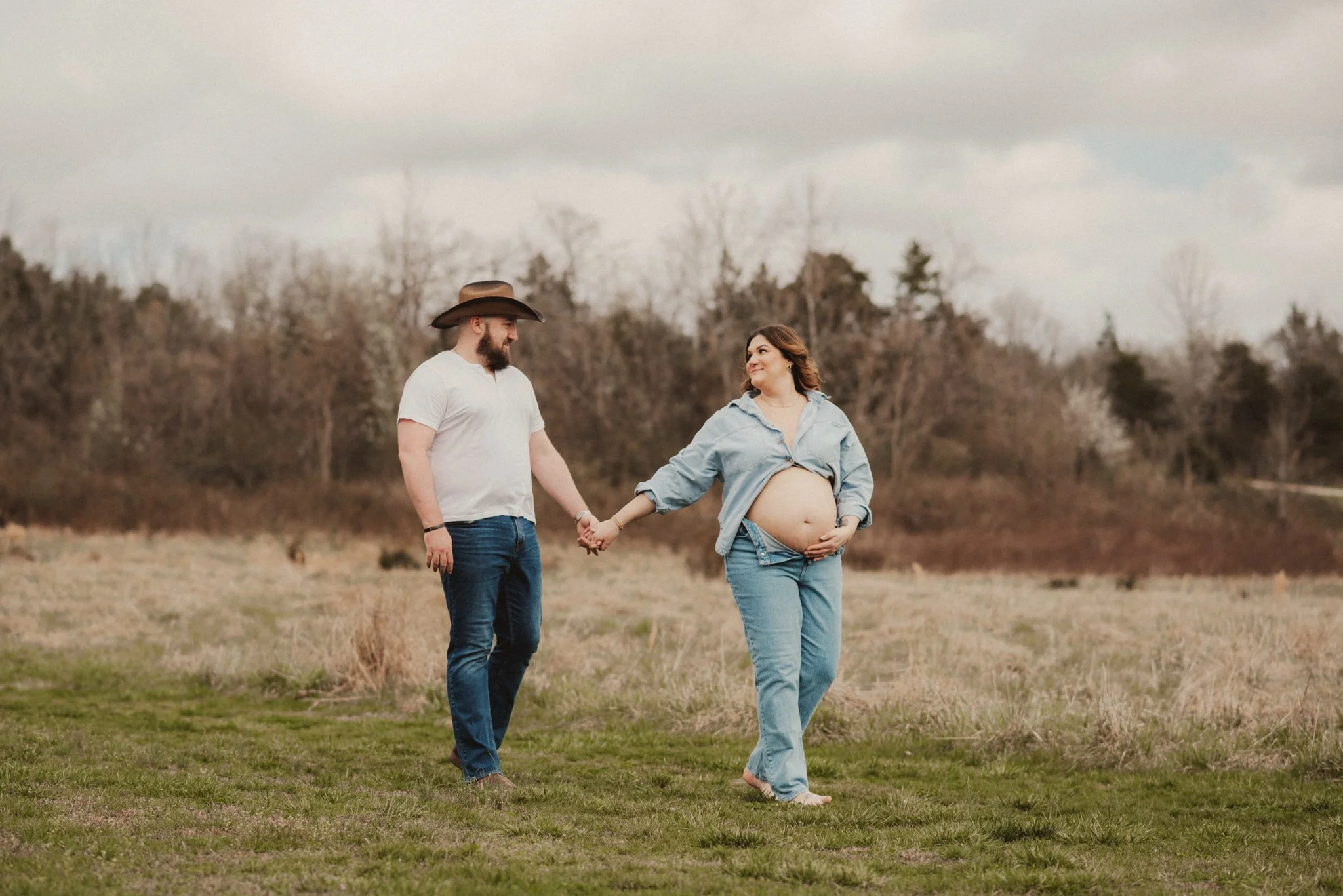 Expecting couple walking together through a field during an outdoor maternity photography session.