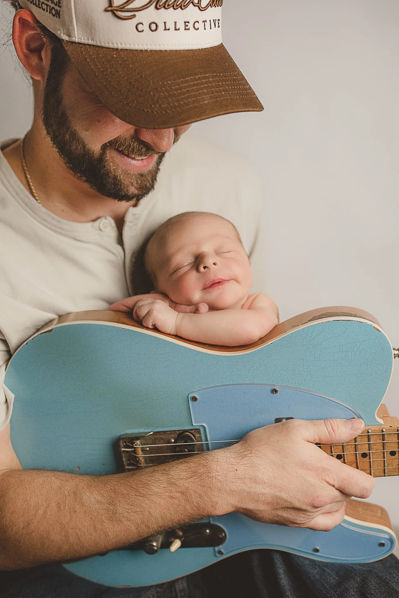 Father holding his sleeping newborn baby with a guitar during a newborn photography session.