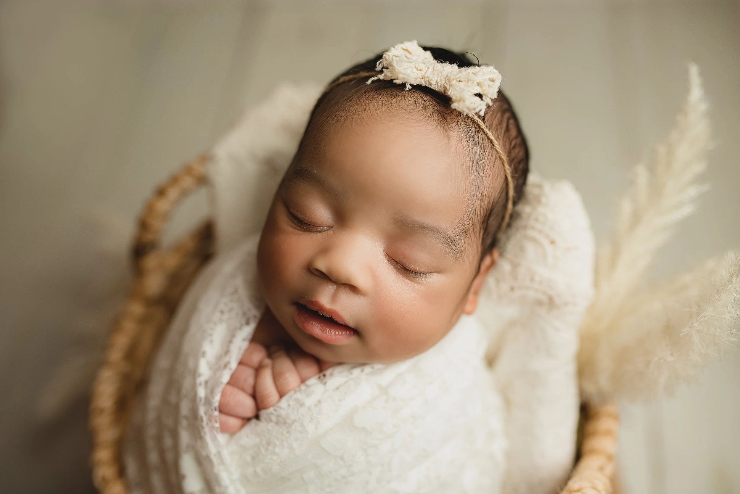 Sleeping newborn baby with a bow wrapped in cream during a posed newborn photography session.