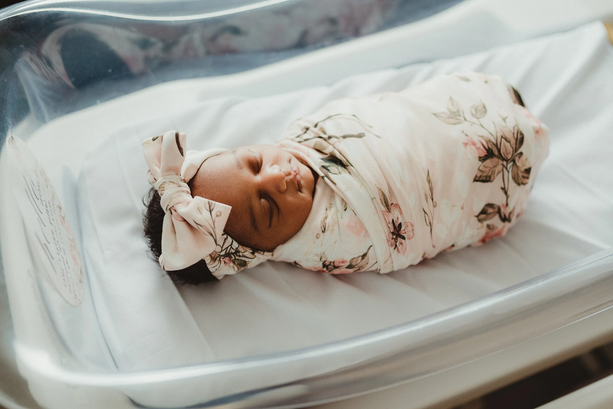 Newborn baby wrapped in a floral blanket in a hospital bassinet during a Fresh 48 photography session.