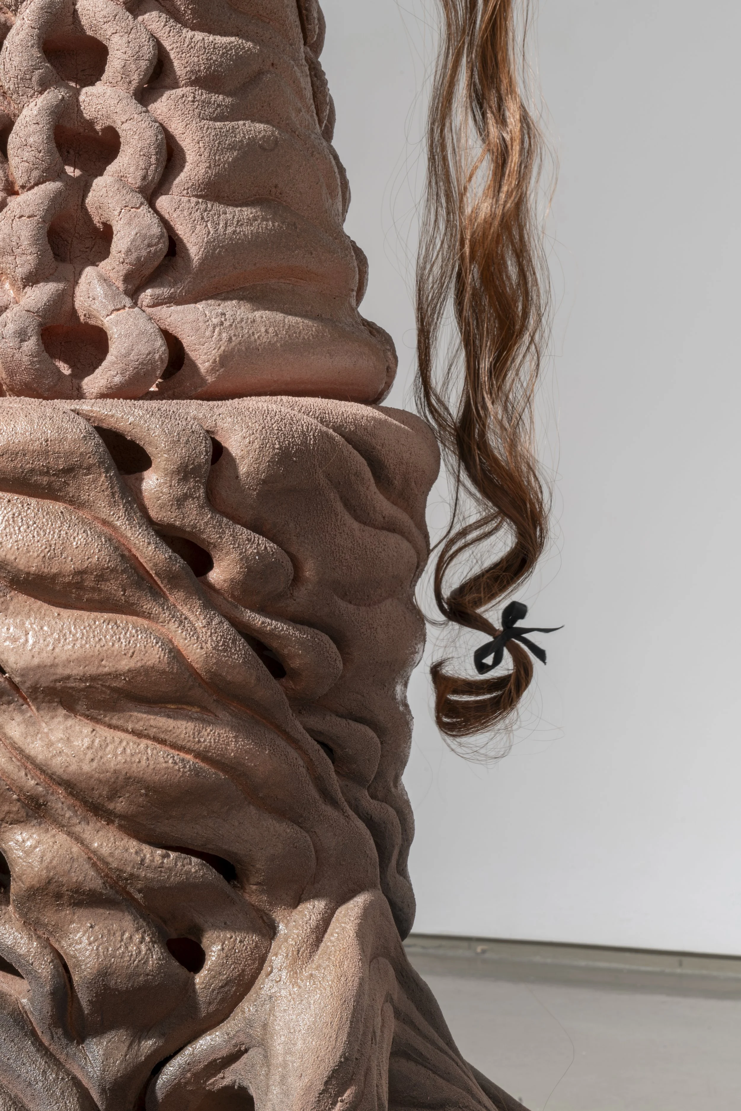 Detail of: French Knitter (A Tube within a tube), 2025. Ceramic, cast aluminum, synthetic hair and polyester ribbon.