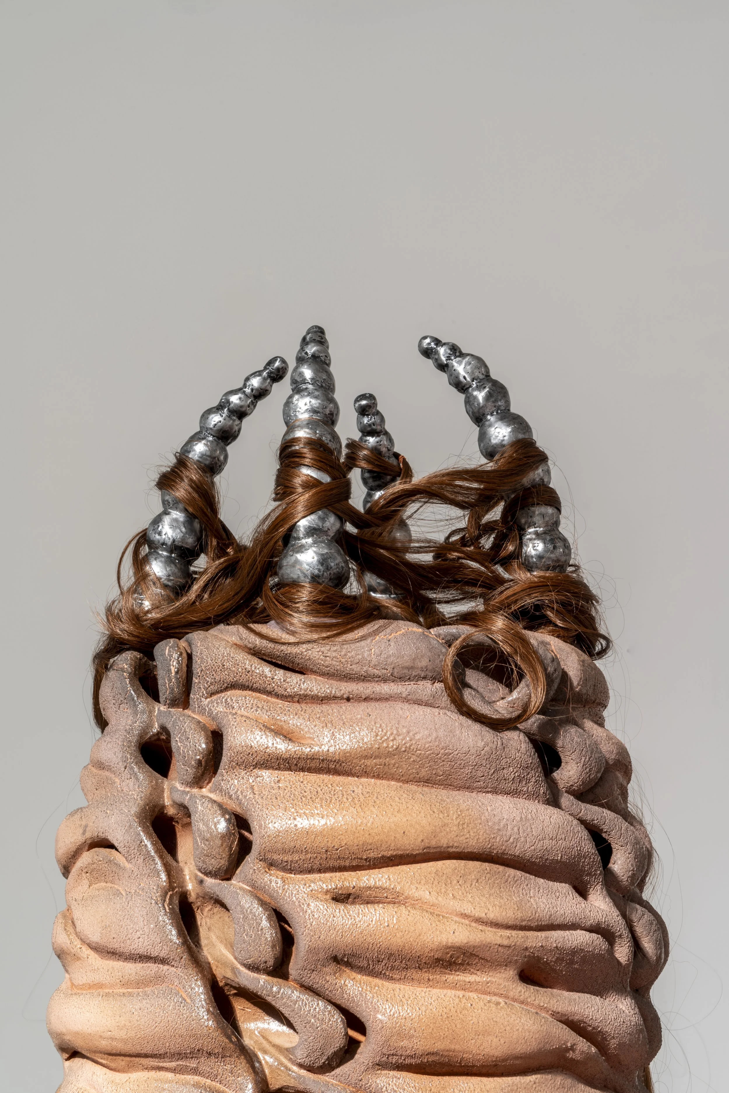 Detail of: French Knitter (A Tube within a tube), 2025. Ceramic, cast aluminum, synthetic hair and polyester ribbon.