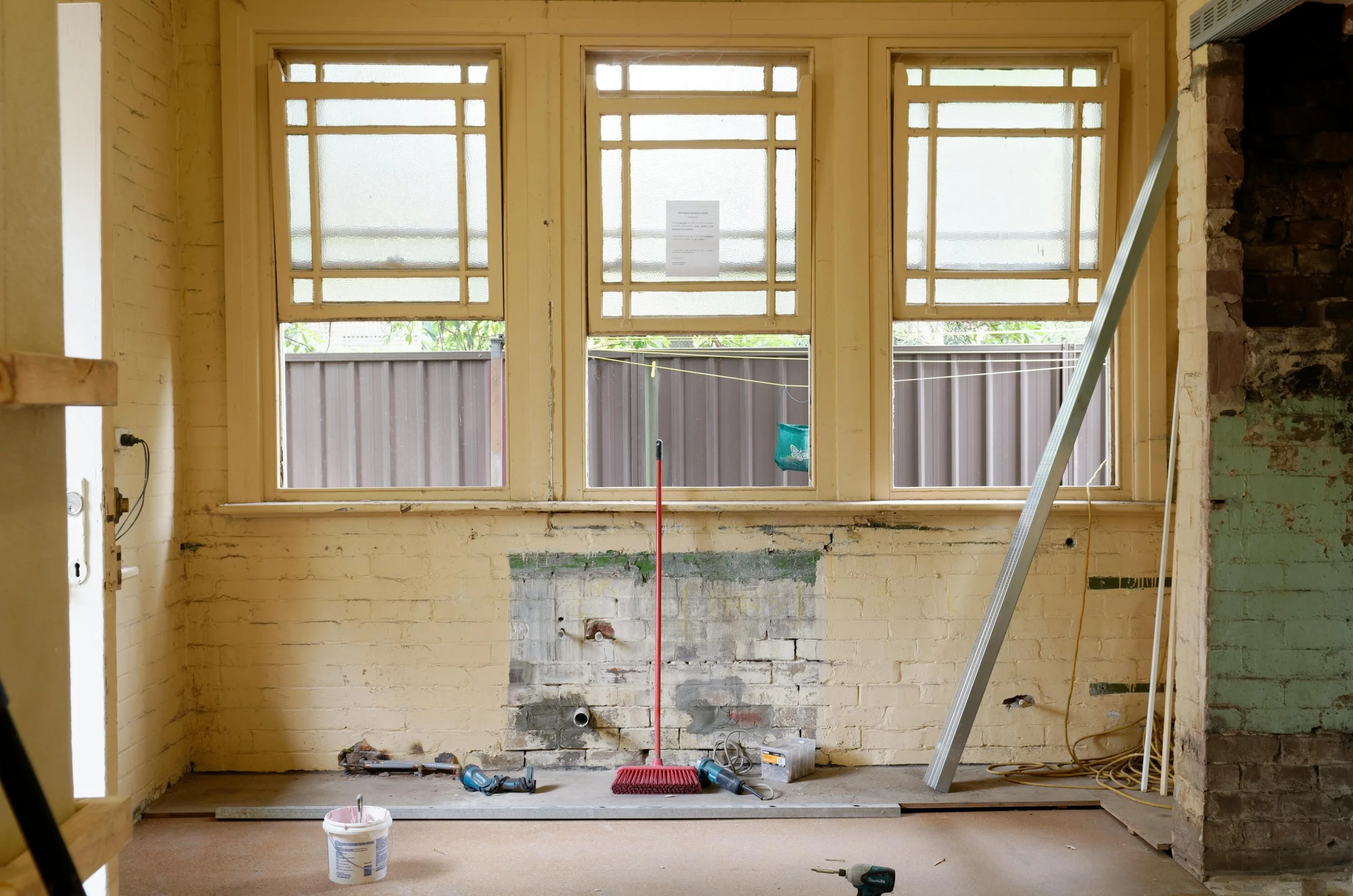 Room under renovation with three large windows, bricks, construction tools, and materials scattered around.