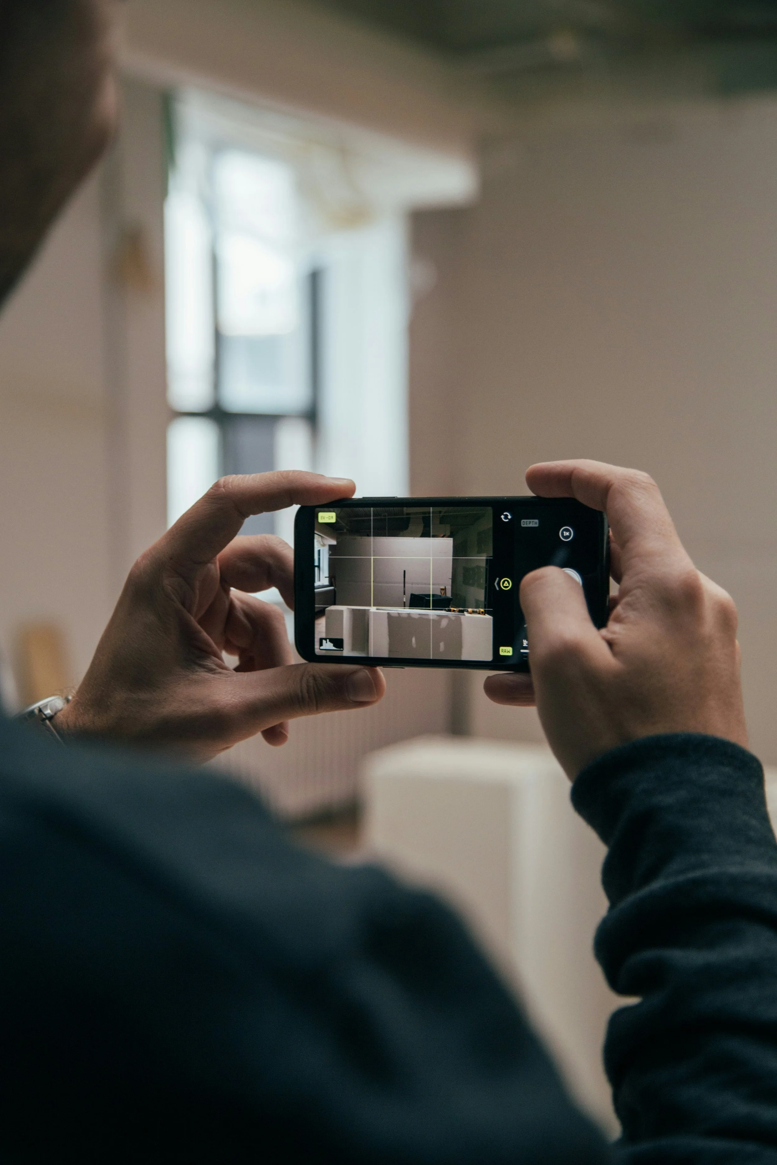 Person taking a photograph of a room interior with a smartphone.