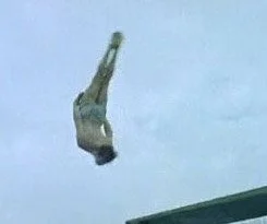 A person falling headfirst from a height in mid-air against a cloudy sky.