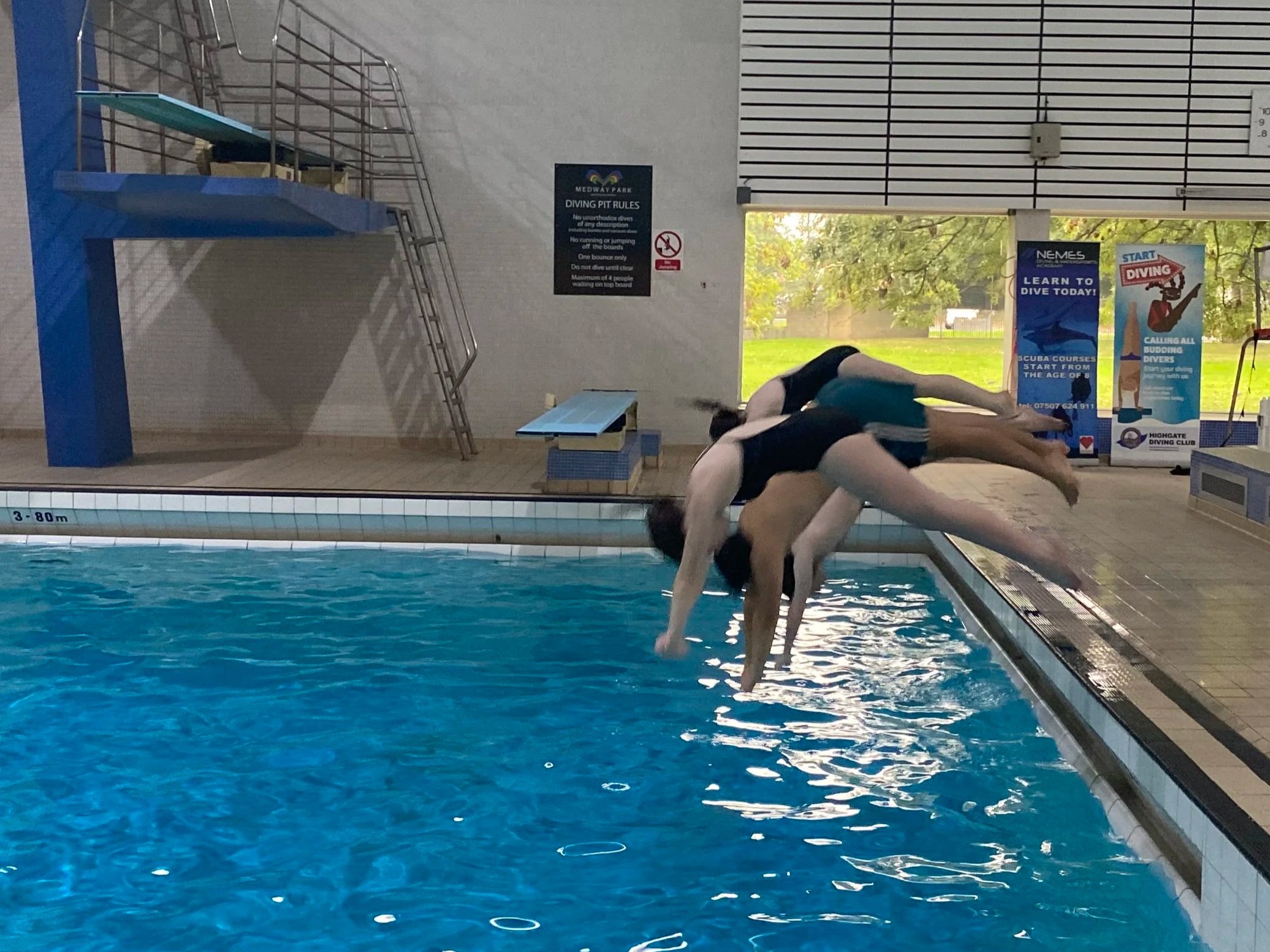 Two people diving into an indoor swimming pool.