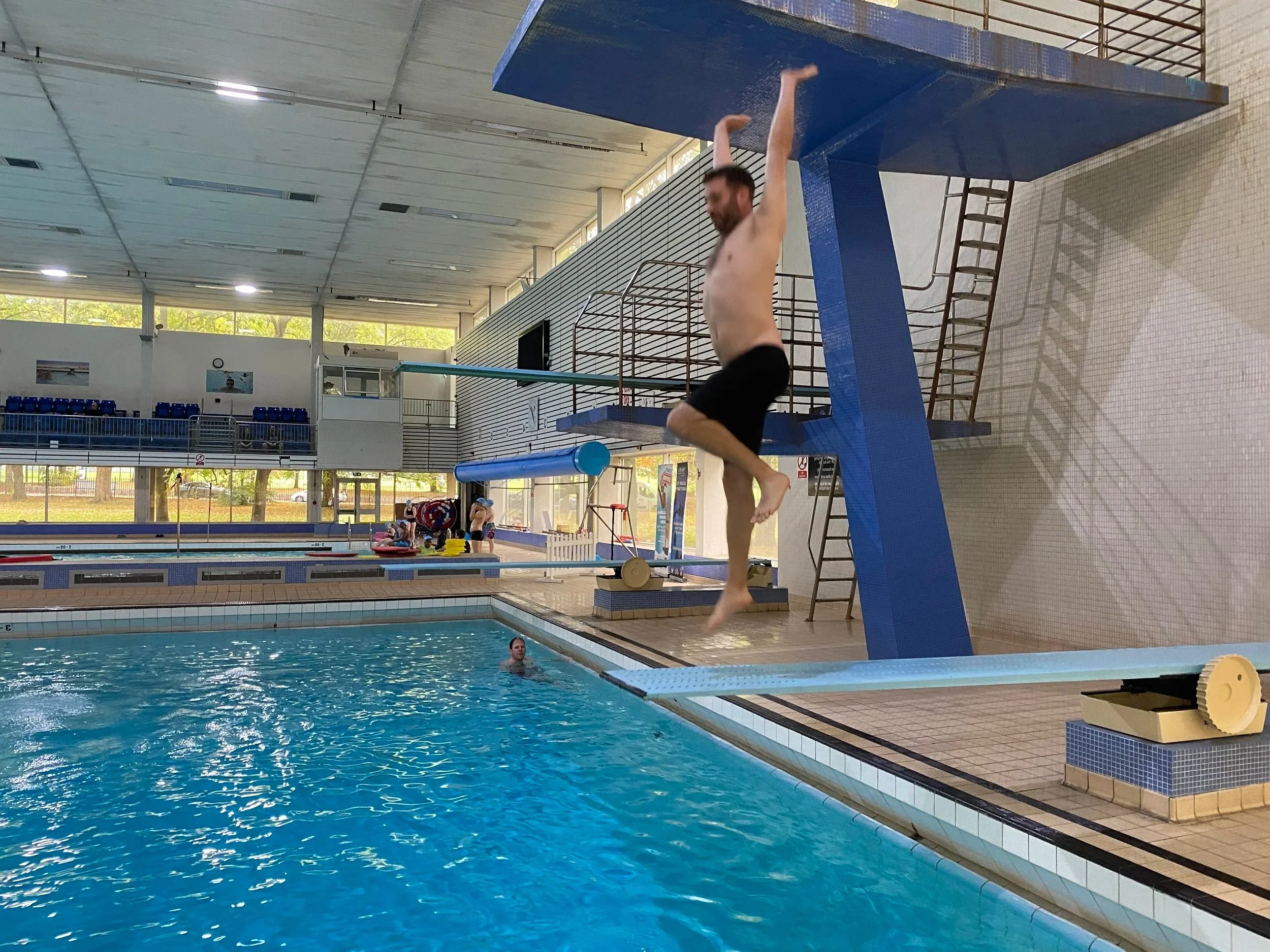 A man is jumping off a diving board into a swimming pool inside an indoor aquatic center.