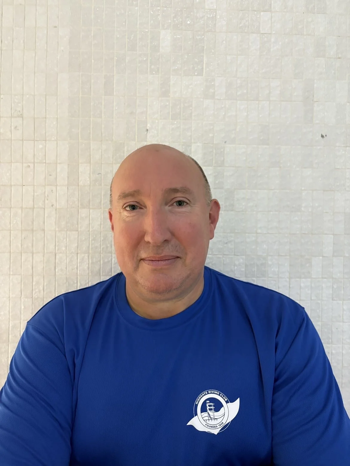 A young man standing confidently with his arms crossed in front of a stone wall, wearing sunglasses, a bandana, a white sleeveless shirt, patterned shorts, and carrying a studded backpack.