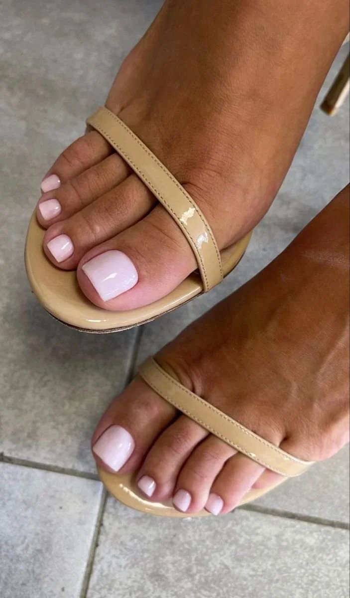 Close-up of a person's feet wearing beige flip-flops with painted toenails on a tiled floor.
