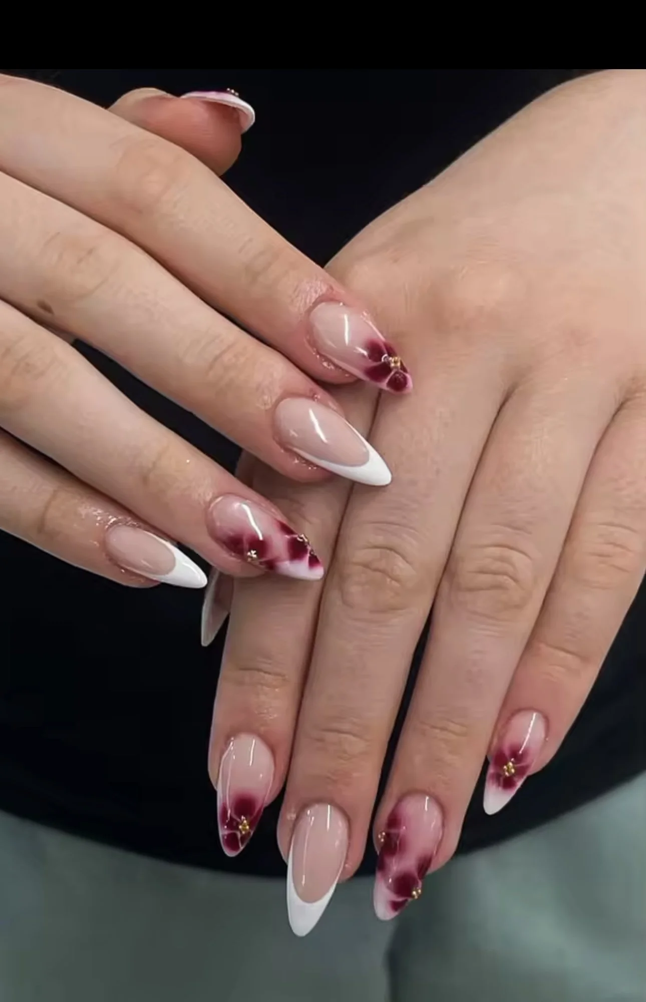 Close-up of hands with manicured nails, featuring a design with white tips, red floral accents, and small gold decorations.