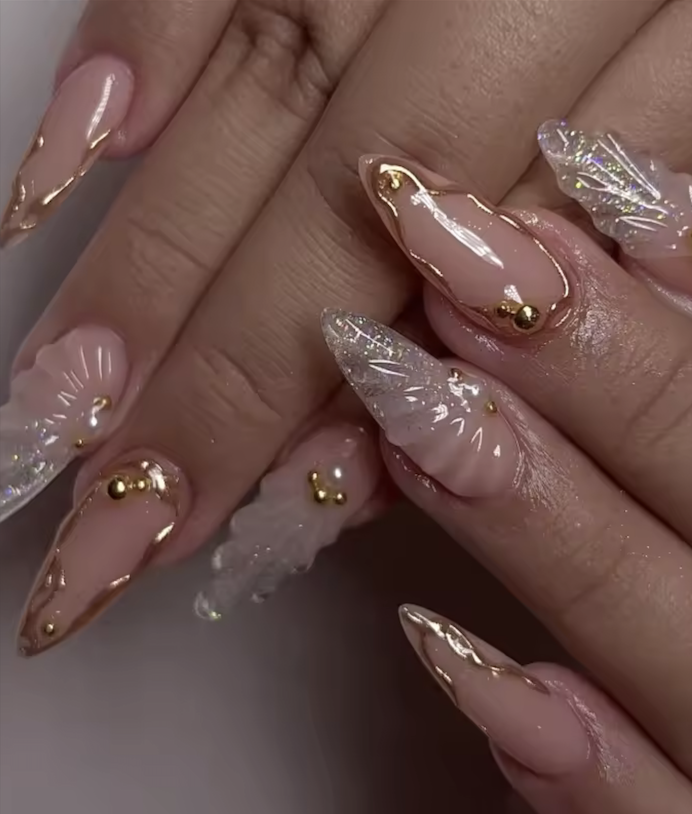 Close-up of manicured nails with pink, white, and gold accents, some featuring 3D pearl details and holographic effects.
