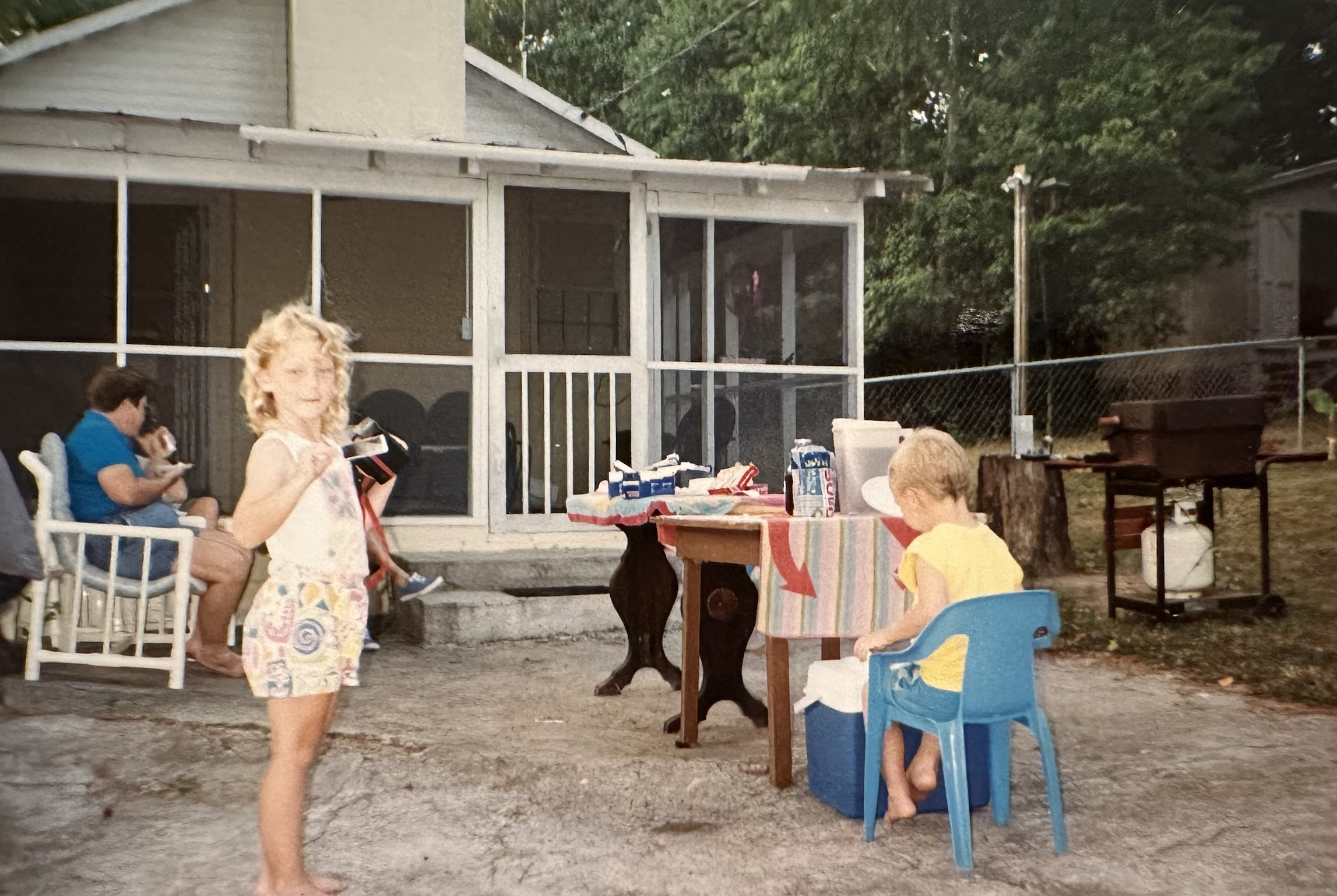 Children and adults at a backyard gathering with outdoor furniture and a screened porch, during dusk.