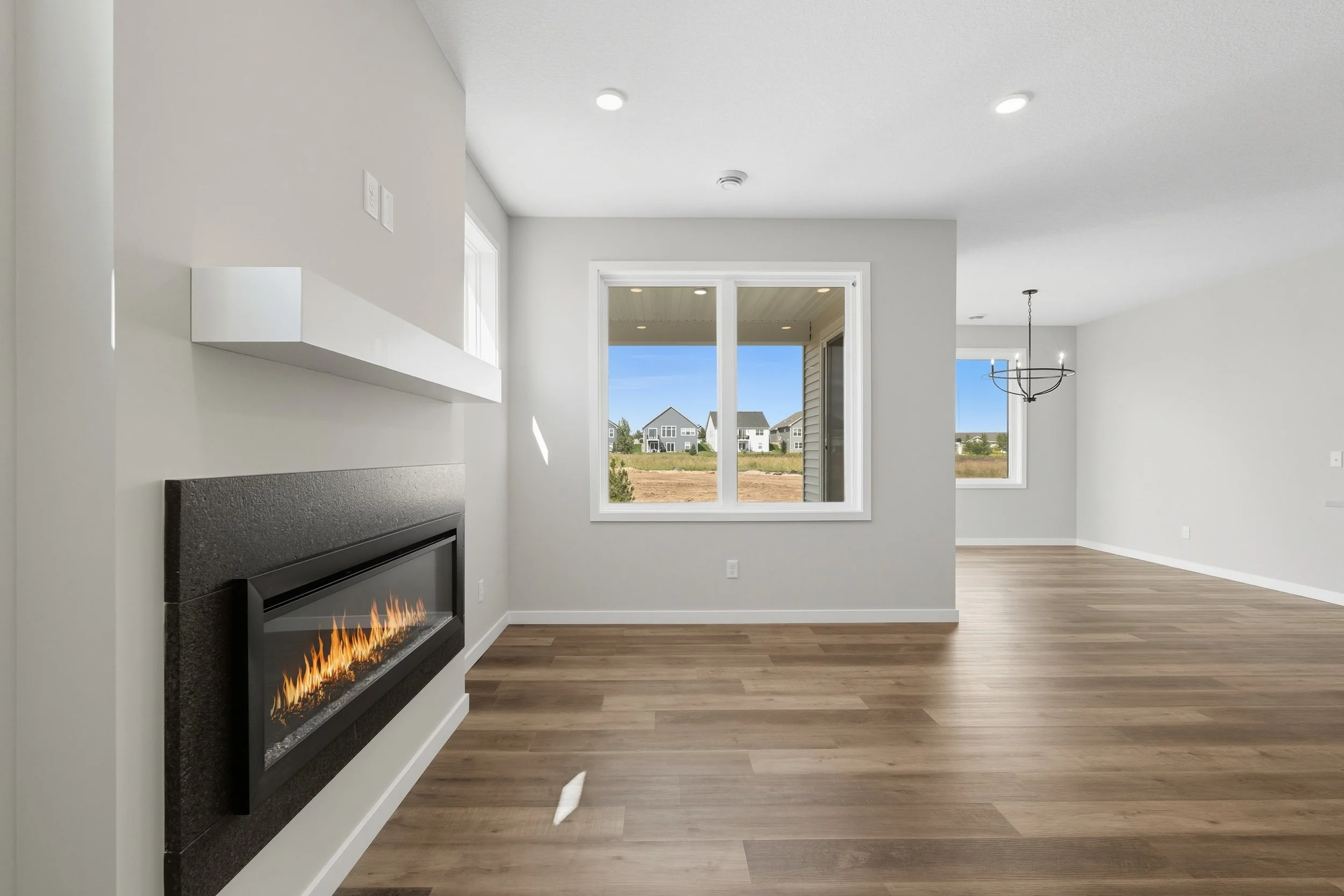 Living room with a fireplace, large windows showing houses outside, and a chandelier in the dining area.