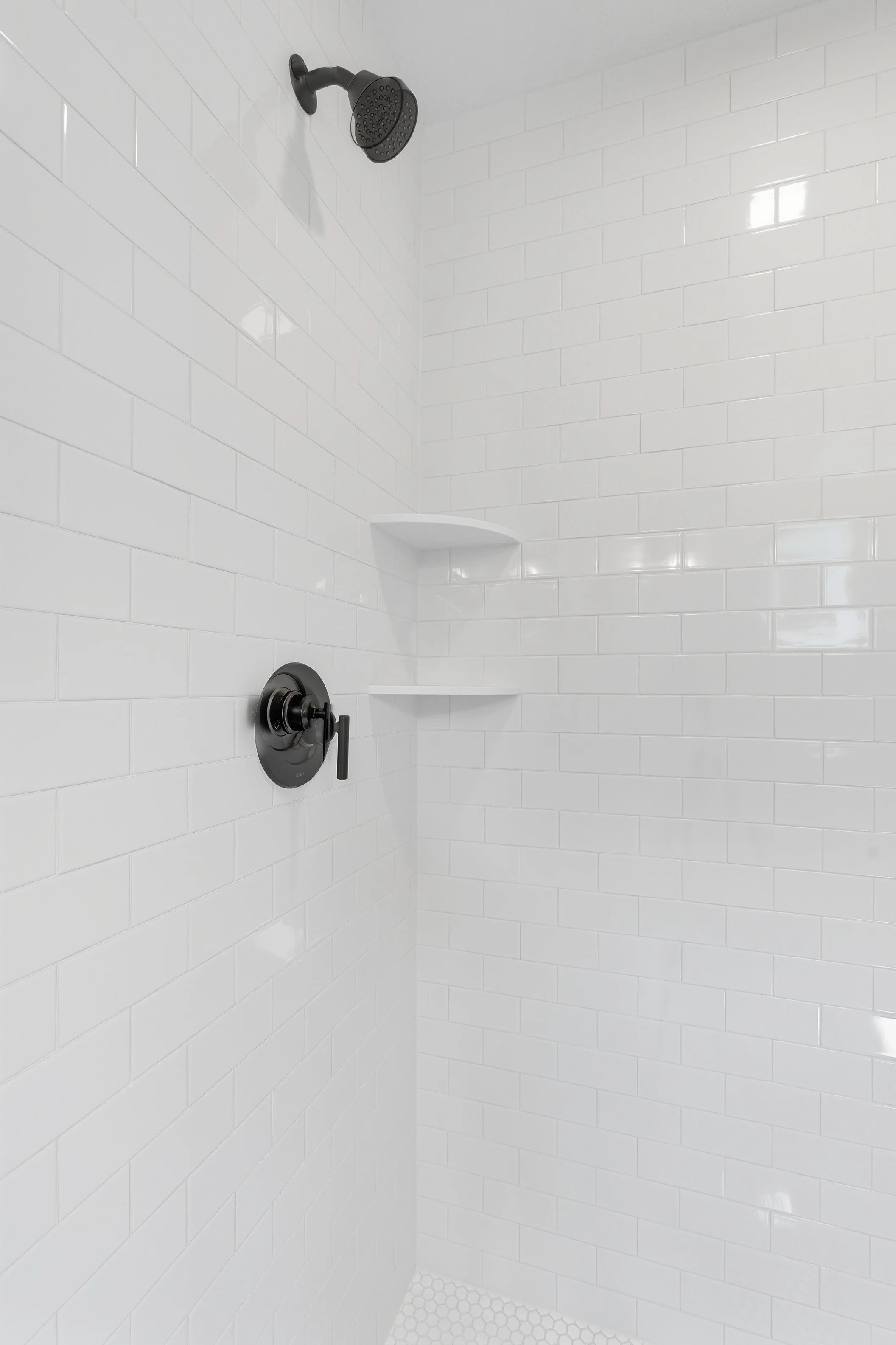 White tiled shower with black showerhead and black handle control.