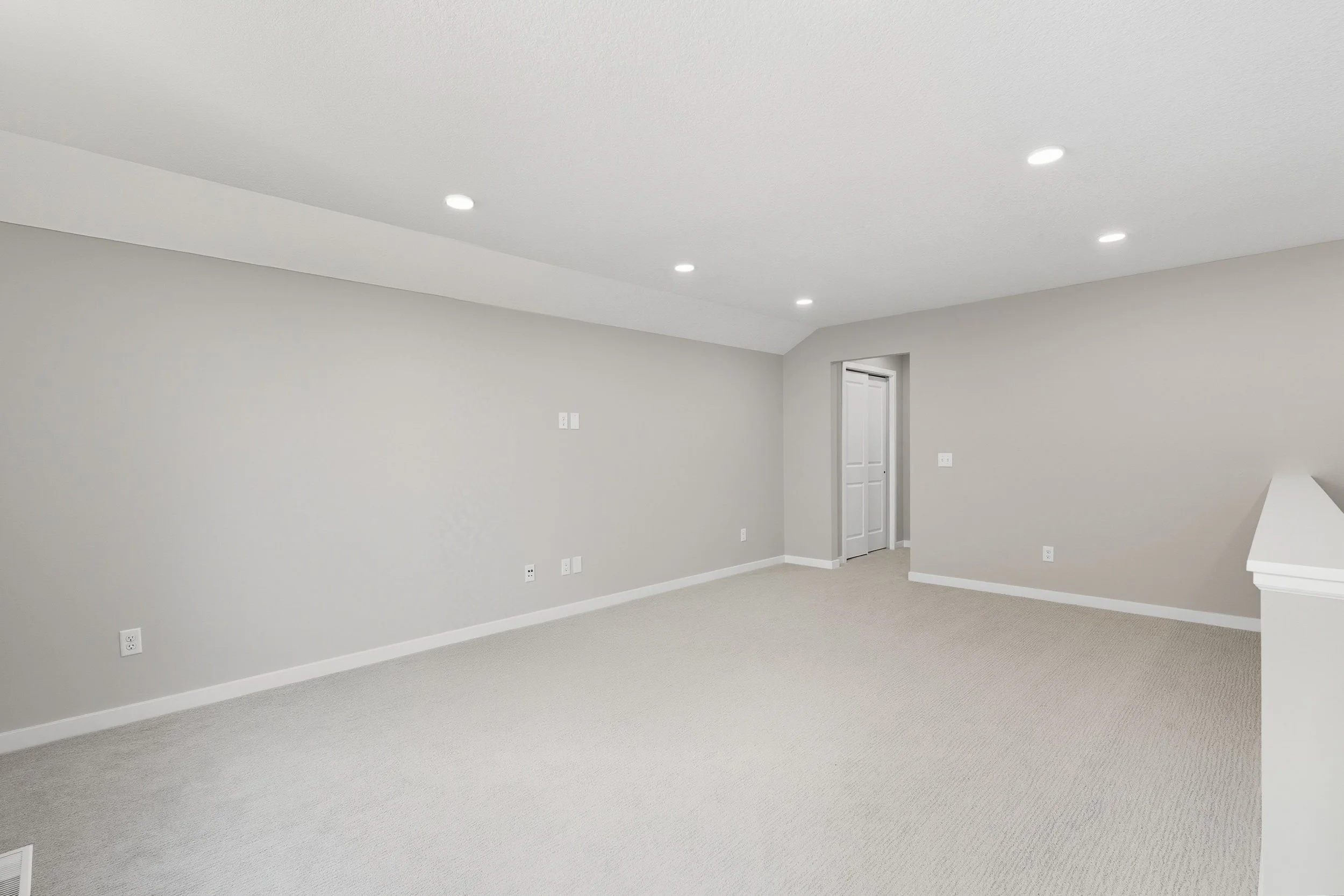Empty room with beige carpet, white walls, and recessed ceiling lights, with a door on the right side.