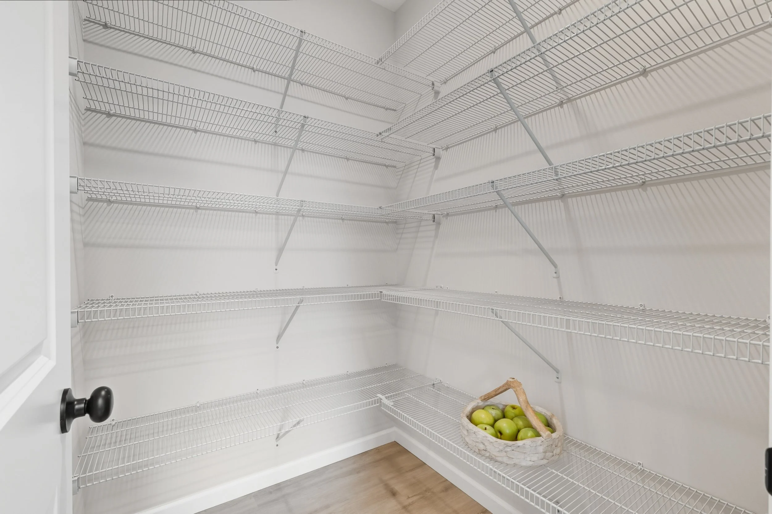 Empty white wire shelving closet with a basket of green apples on the bottom shelf.