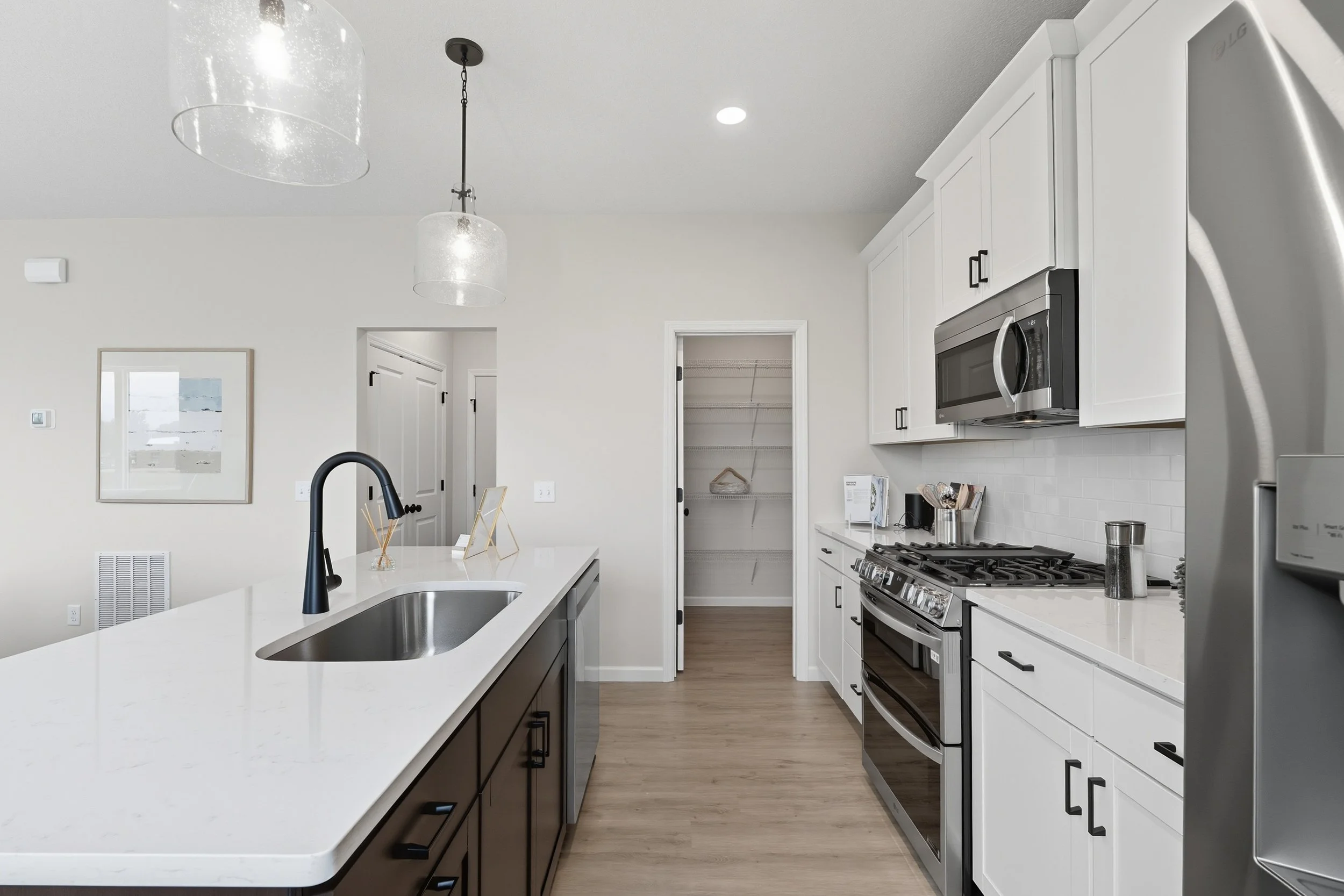 Modern kitchen with white upper cabinets, black hardware, stainless steel appliances, a large island with a white countertop and dark base, and light wood flooring.