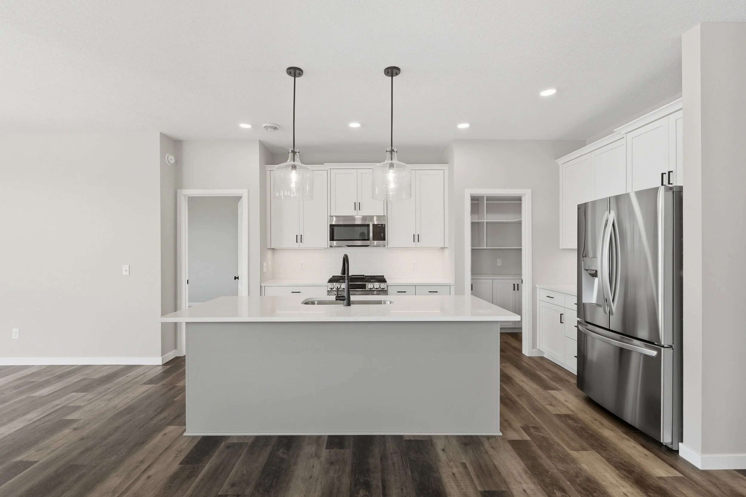 Modern kitchen with white cabinets, stainless steel appliances, a large island with a sink, pendant lights, and dark wood flooring.