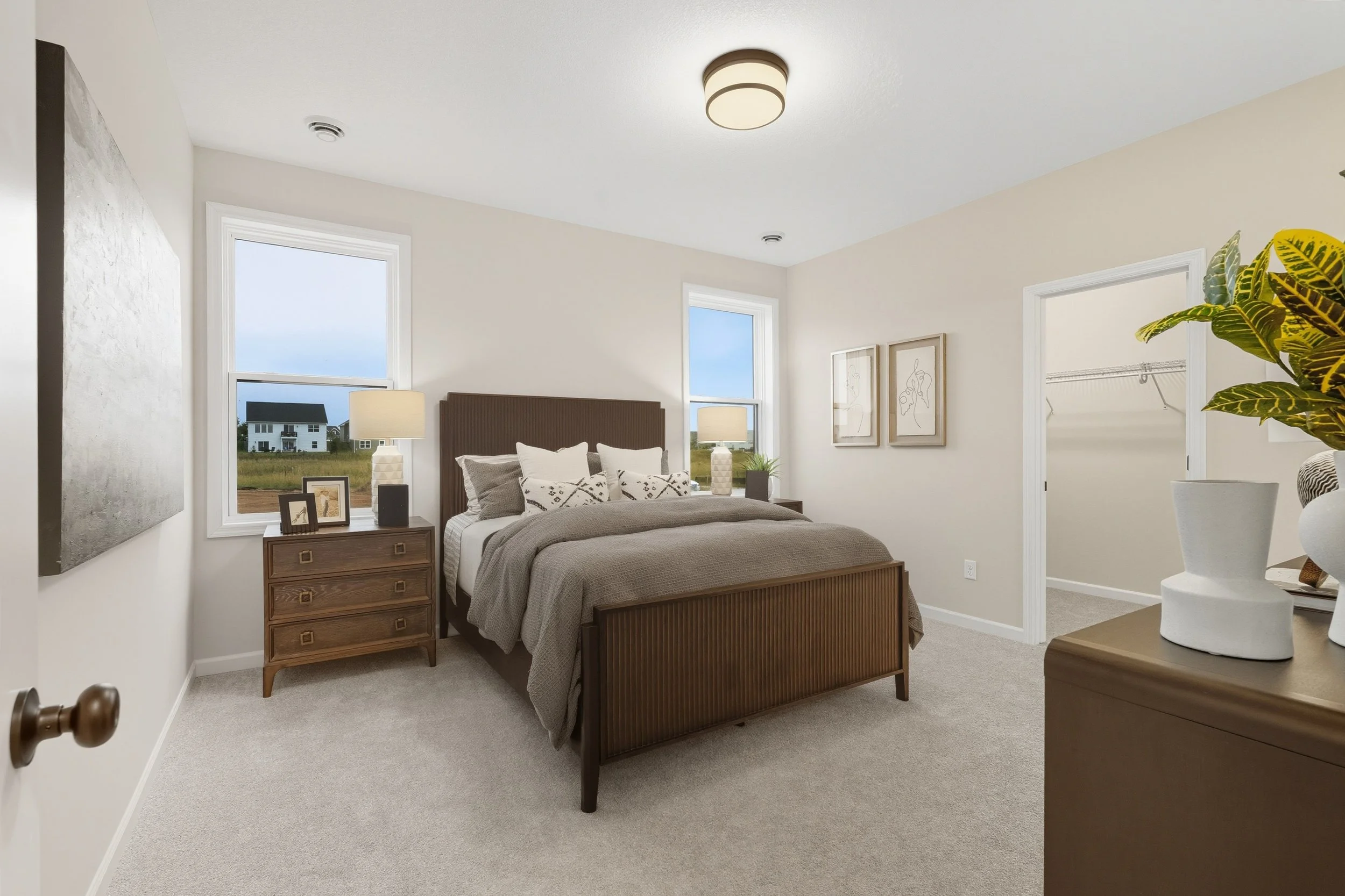 A cozy bedroom with a bed, nightstand, lamps, artwork, and a walk-in closet.