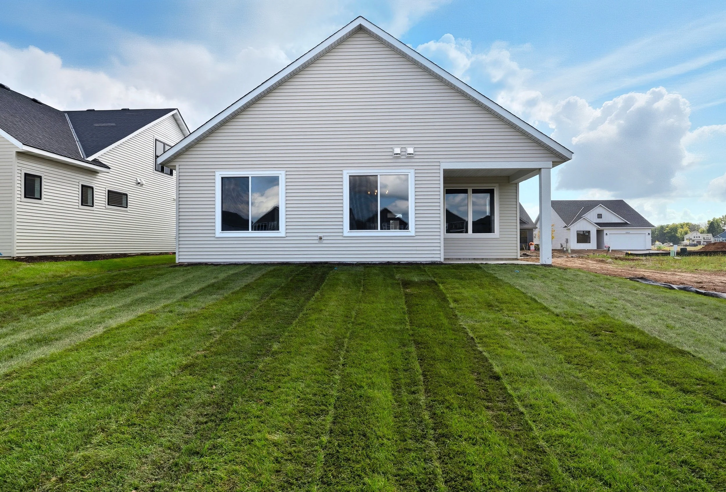 Newly built white house with a manicured green lawn, large windows, and a small covered porch on the right side, under a partly cloudy sky.