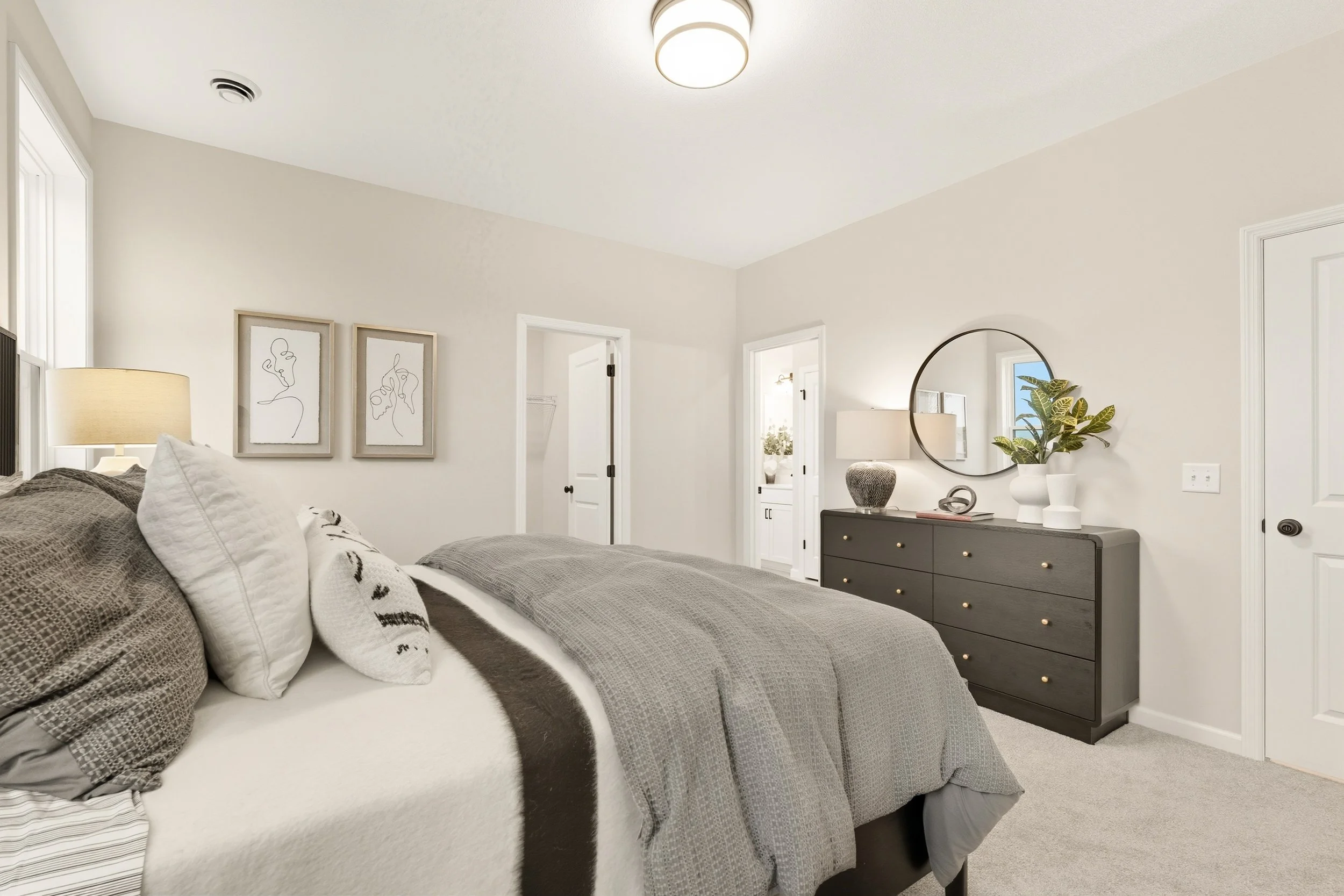 Contemporary bedroom with bed, gray bedding, framed artwork, dresser with mirror, decorative items, and potted plant