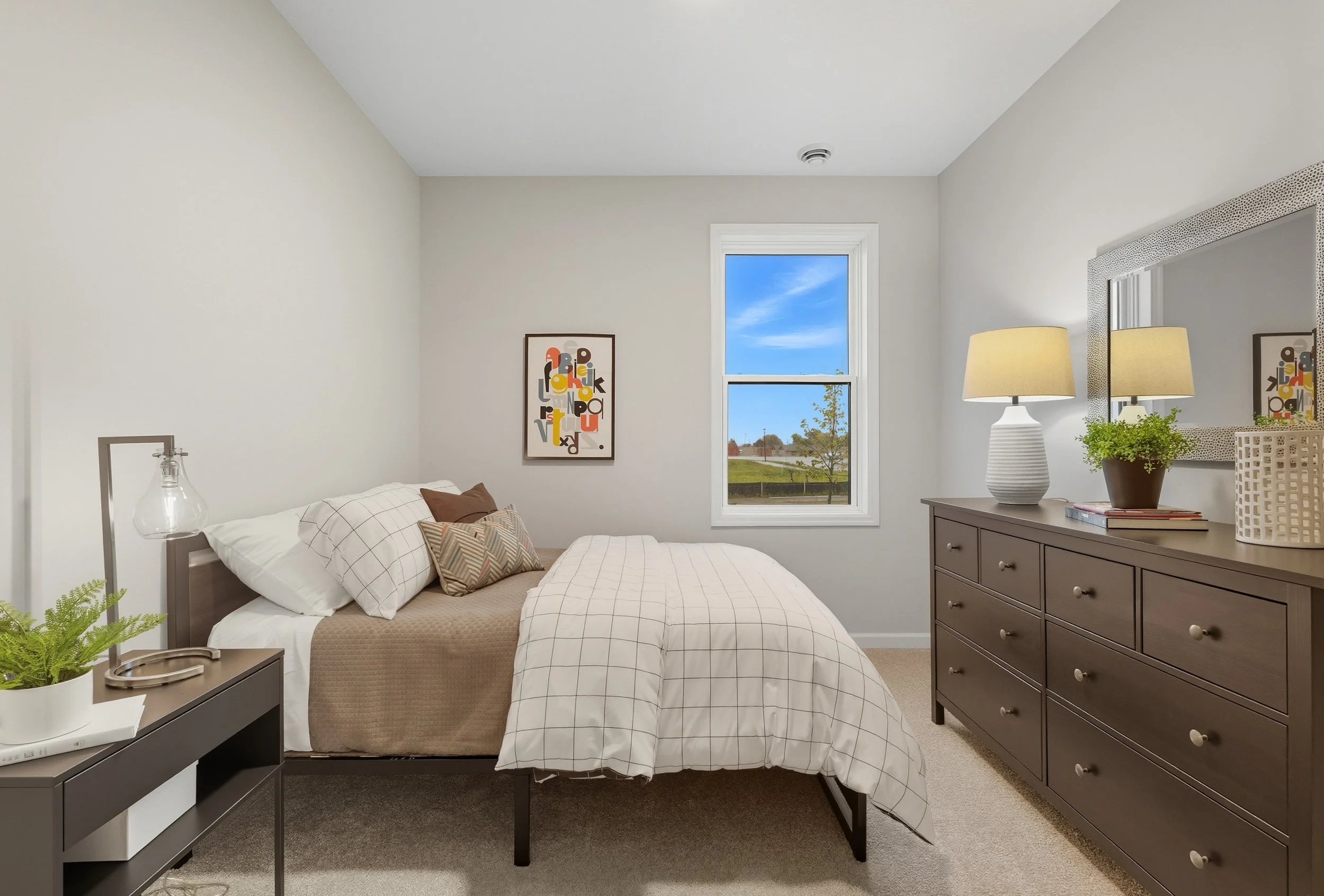 A bedroom with a bed, nightstand, dresser, mirror, and window showing a view of trees and blue sky.