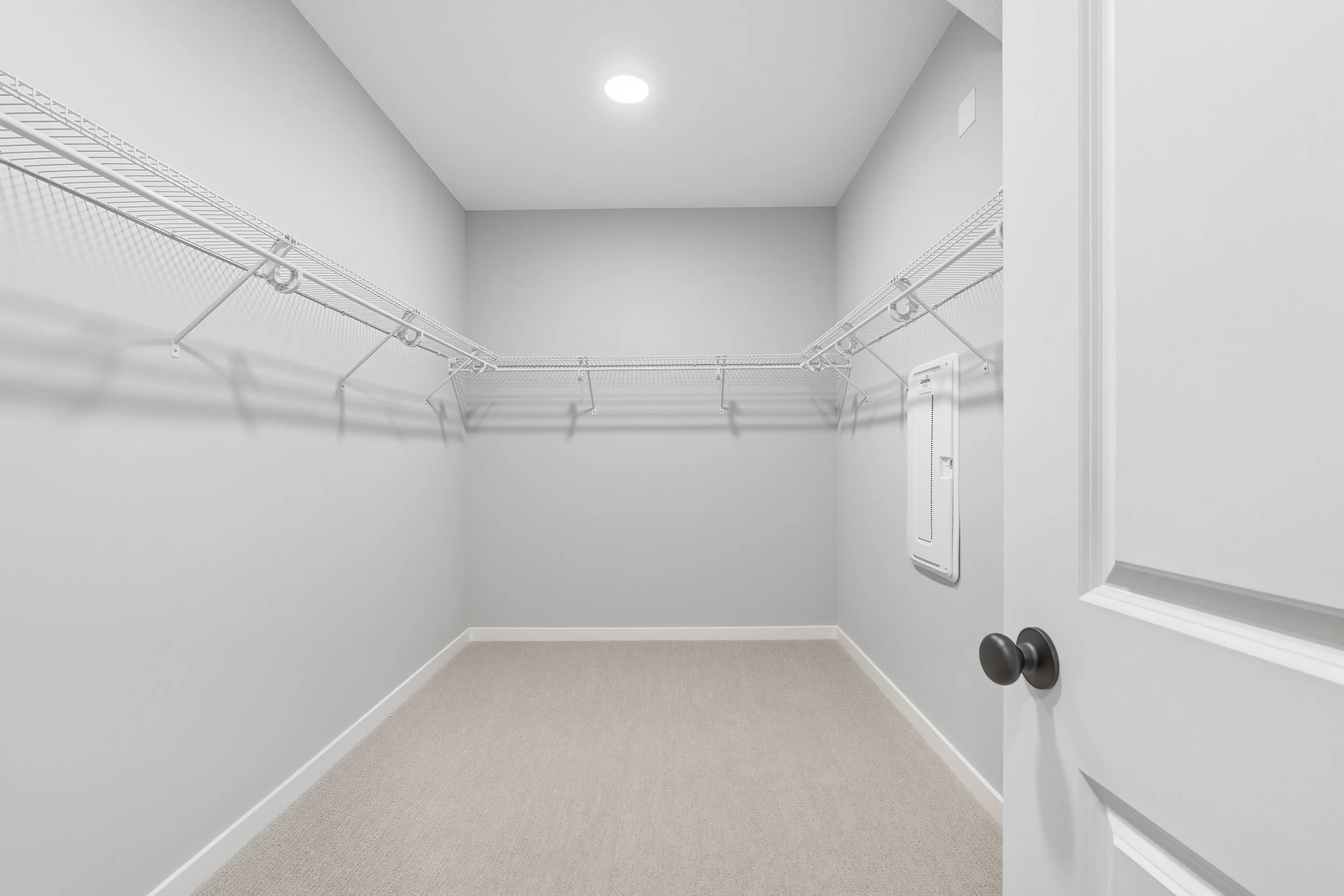 Empty walk-in closet with white wire shelves on both sides, carpeted floor, and white walls.