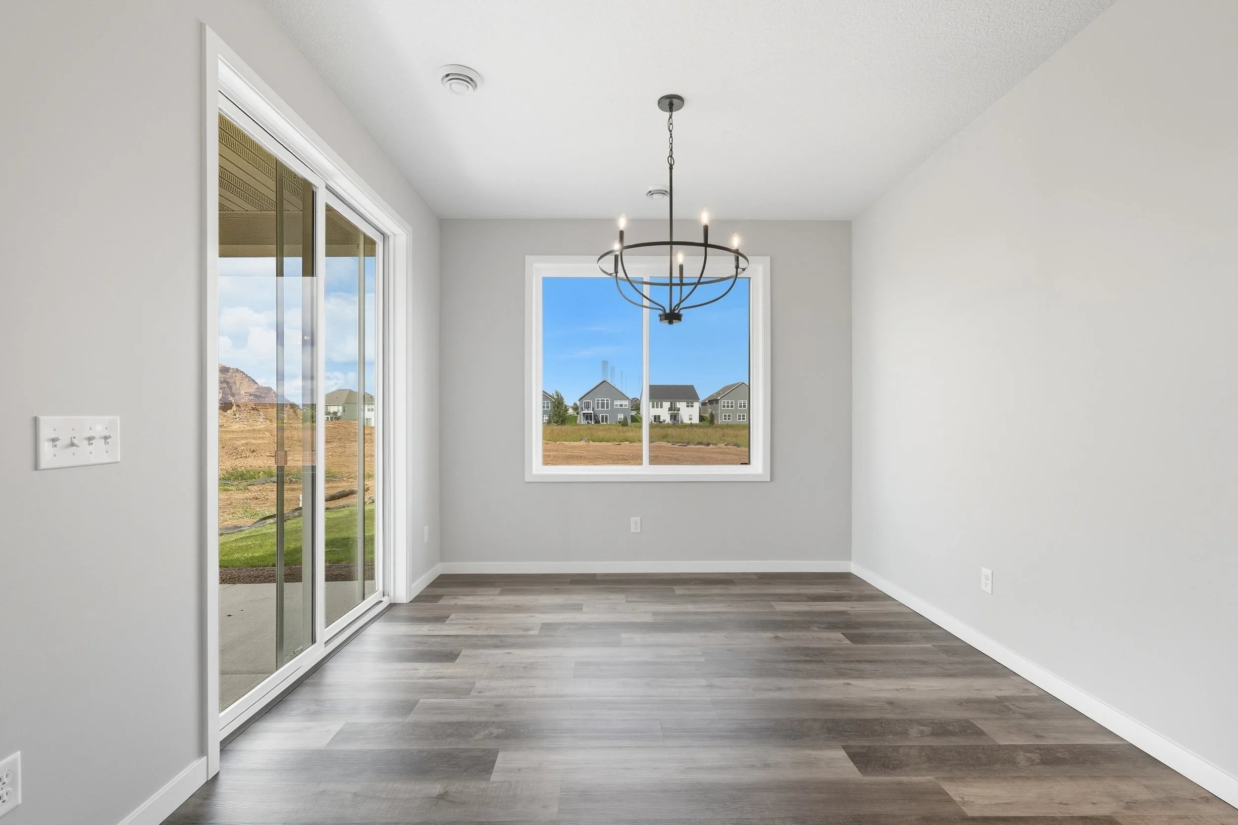 Empty room with a chandelier, sliding glass door, and window showing outdoor houses and blue sky.