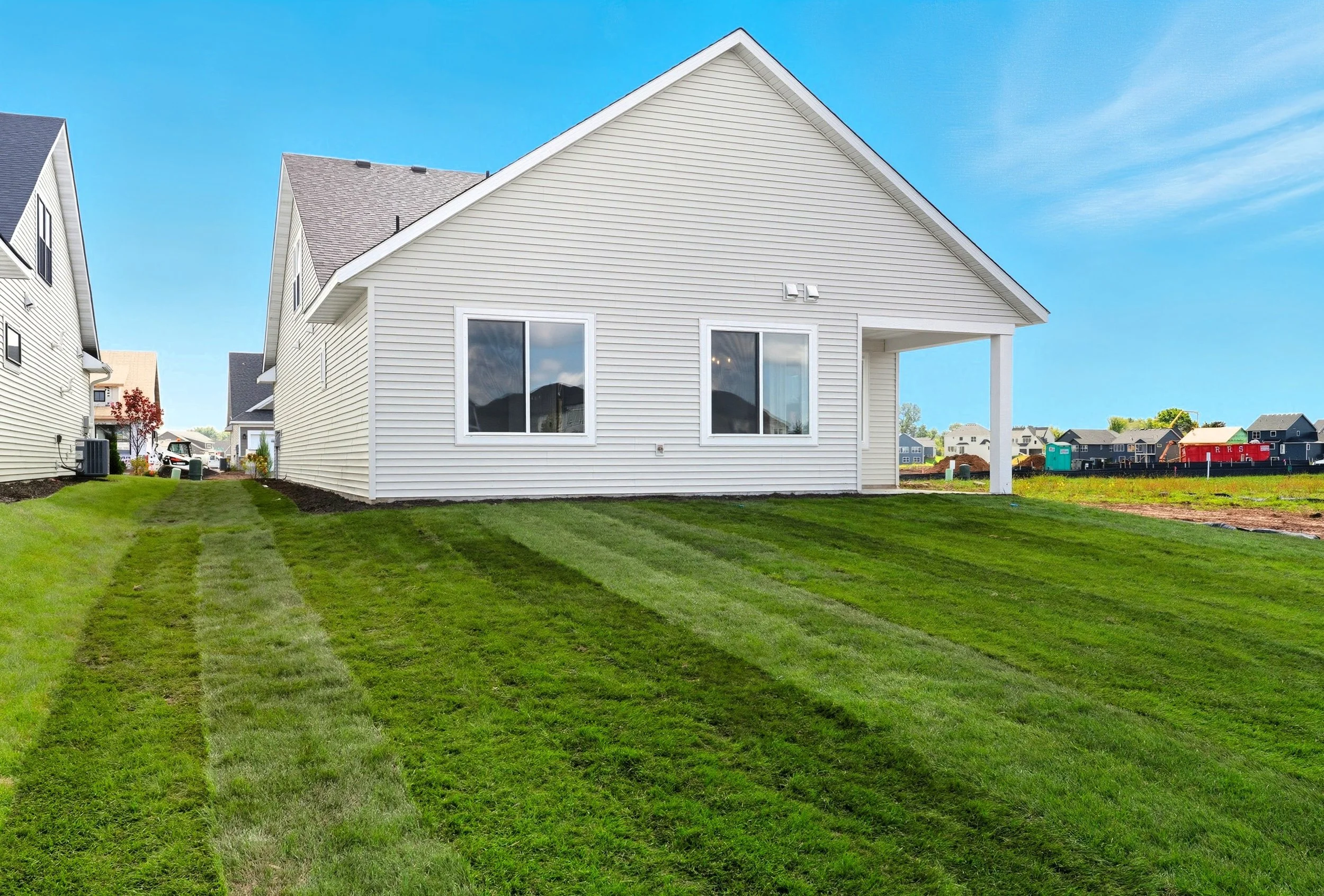 A white house with horizontal siding, two windows, and a covered porch on a grassy lawn under a blue sky.