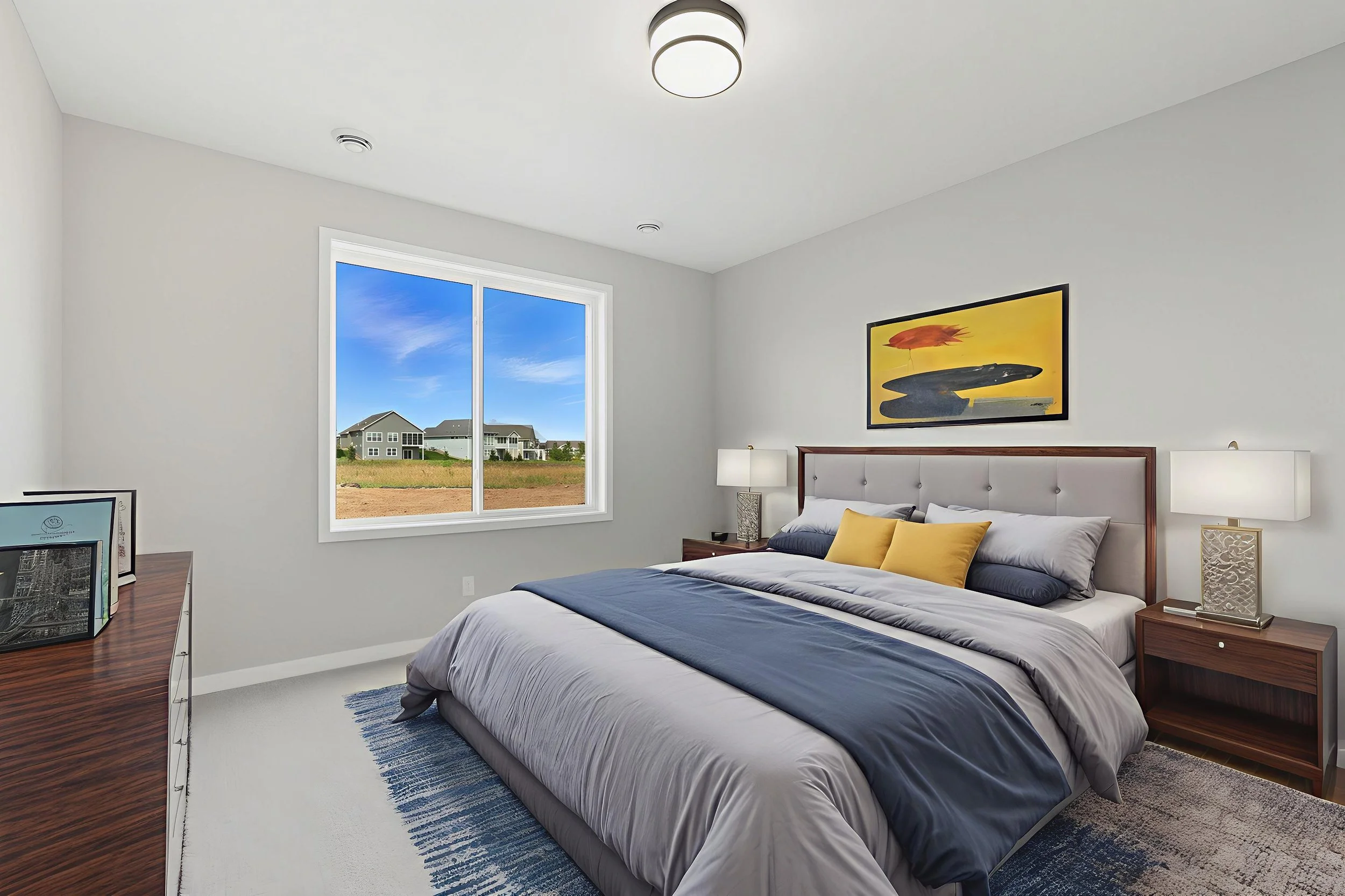 A modern bedroom with a large bed, nightstands with lamps, a colorful abstract painting above the bed, a window showing a view of a grassy yard and neighboring houses, and a wooden dresser with framed pictures or artwork.