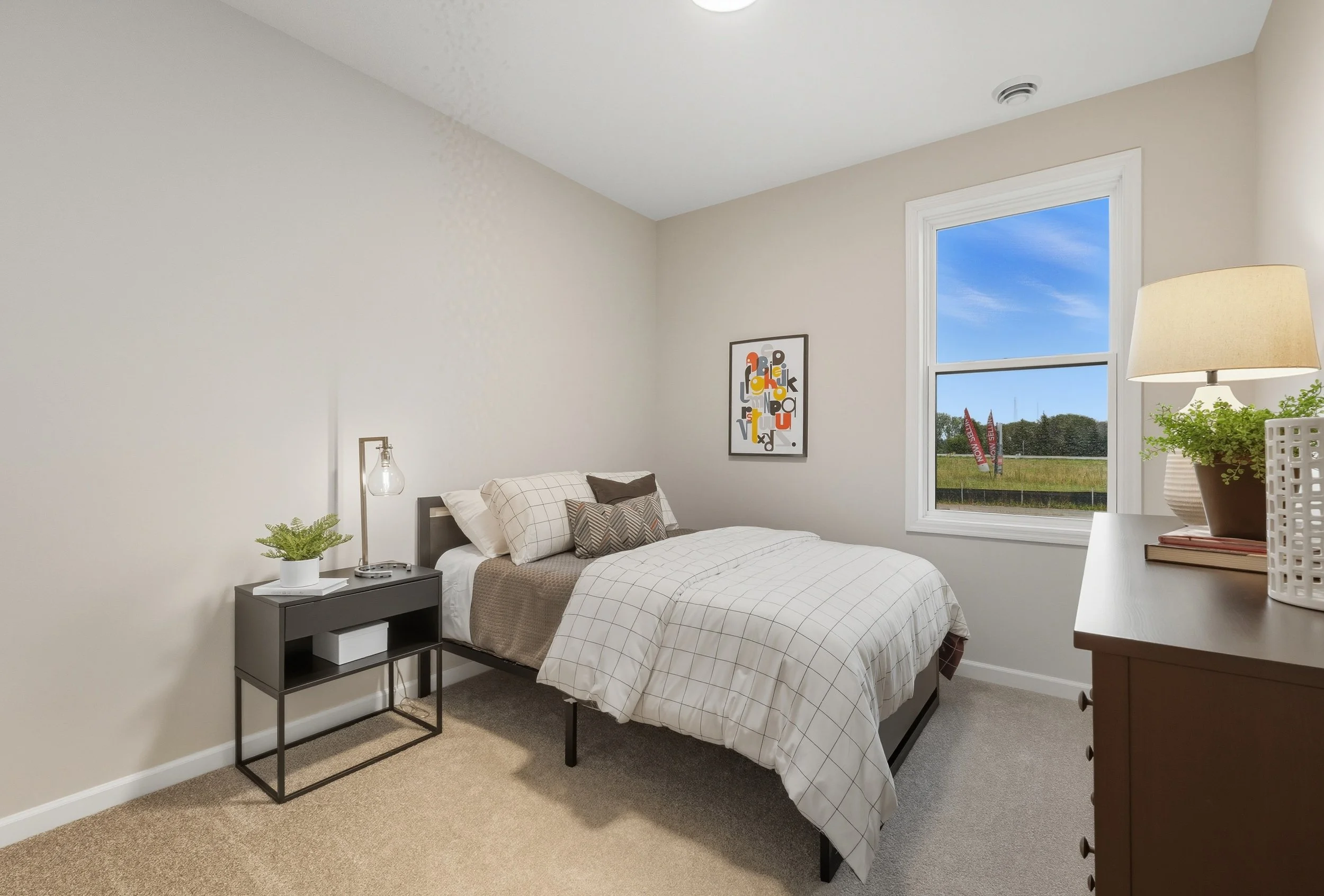 A bedroom with a bed, a nightstand, a dresser, and a window showing a field outside.