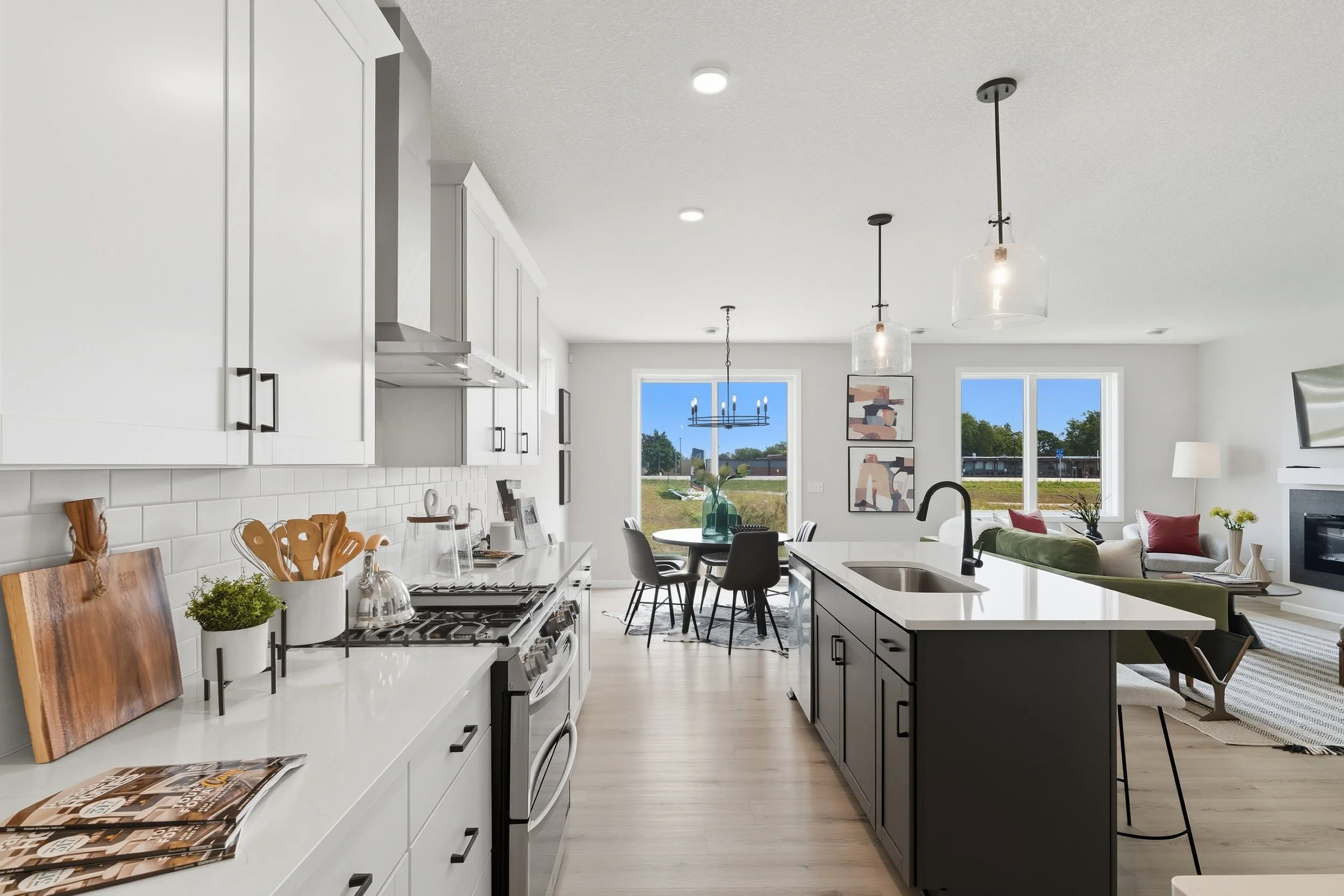 Open-concept kitchen and living room with white cabinetry, black island, dining table, and seating area with windows and outdoor view.
