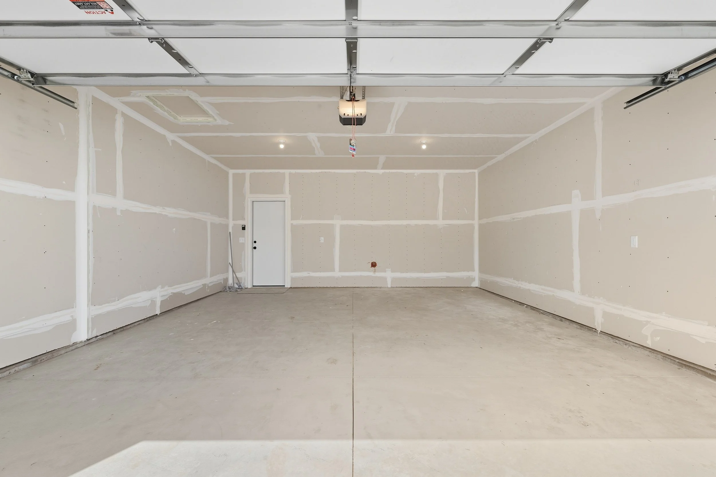 Empty residential garage with unfinished drywall and concrete floor.