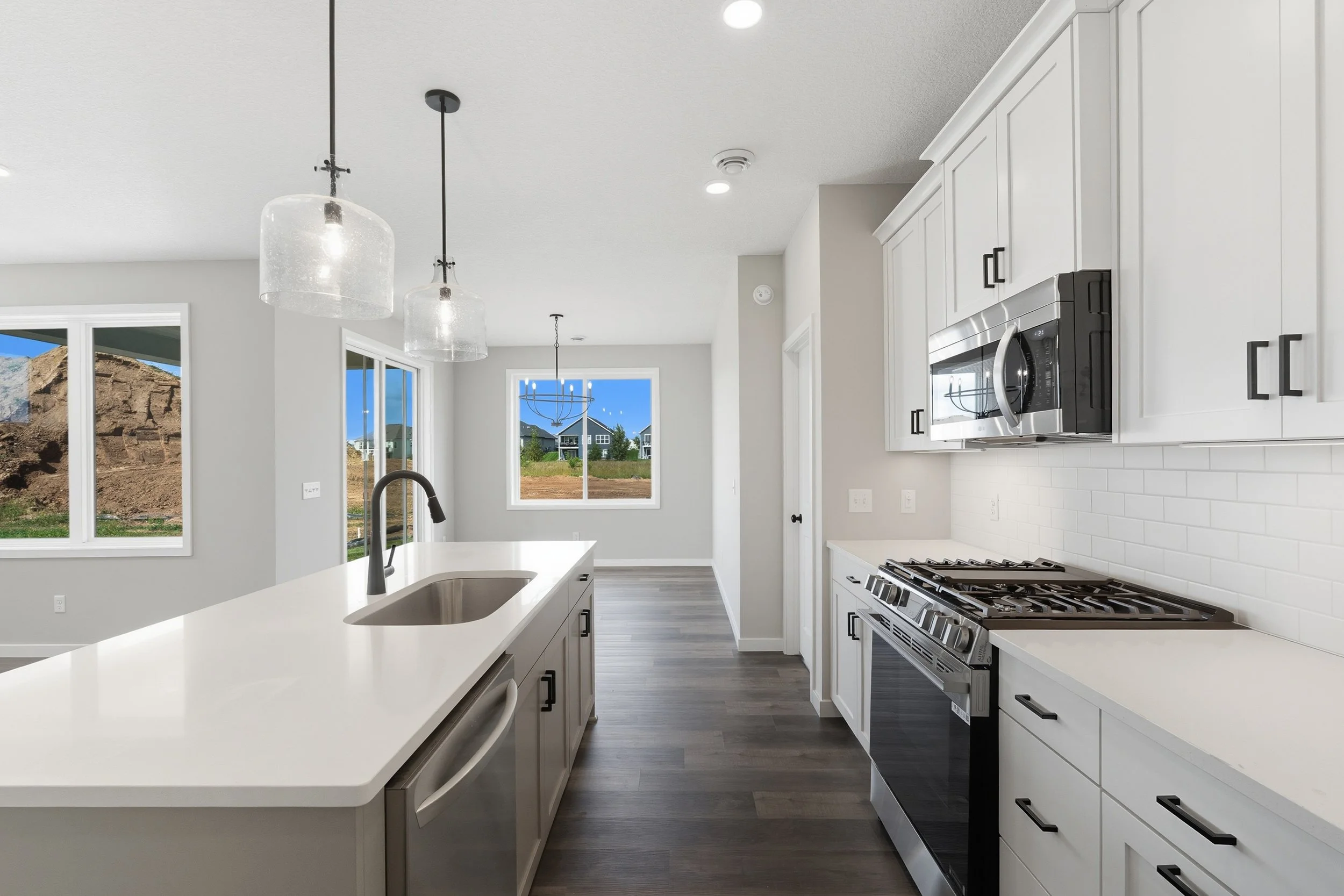 Modern kitchen with white cabinets, stainless steel appliances, and a central island with a sink, featuring large windows showing an outdoor view.