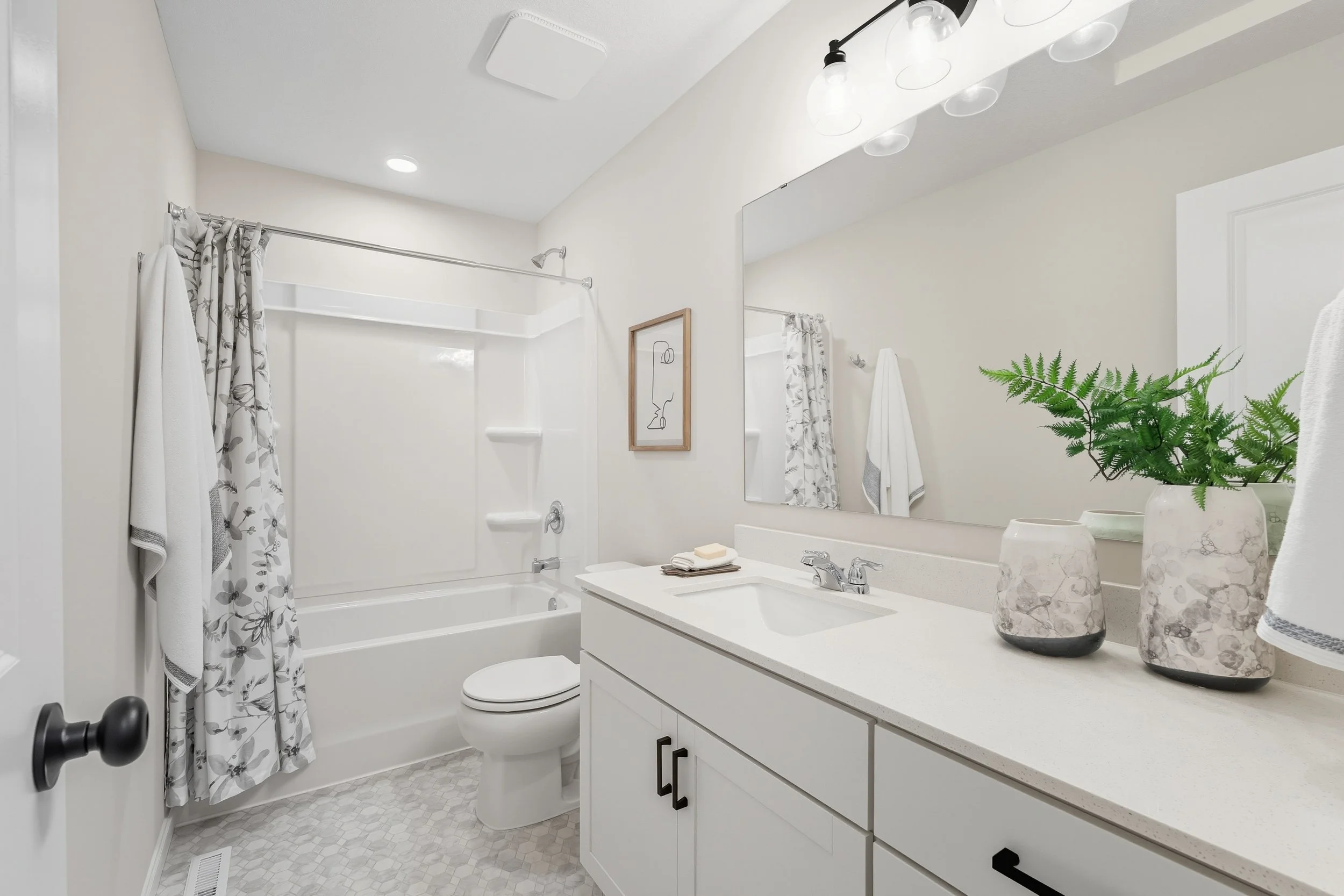 Bright bathroom with white vanity, large mirror, potted plant, and bathtub with shower curtain