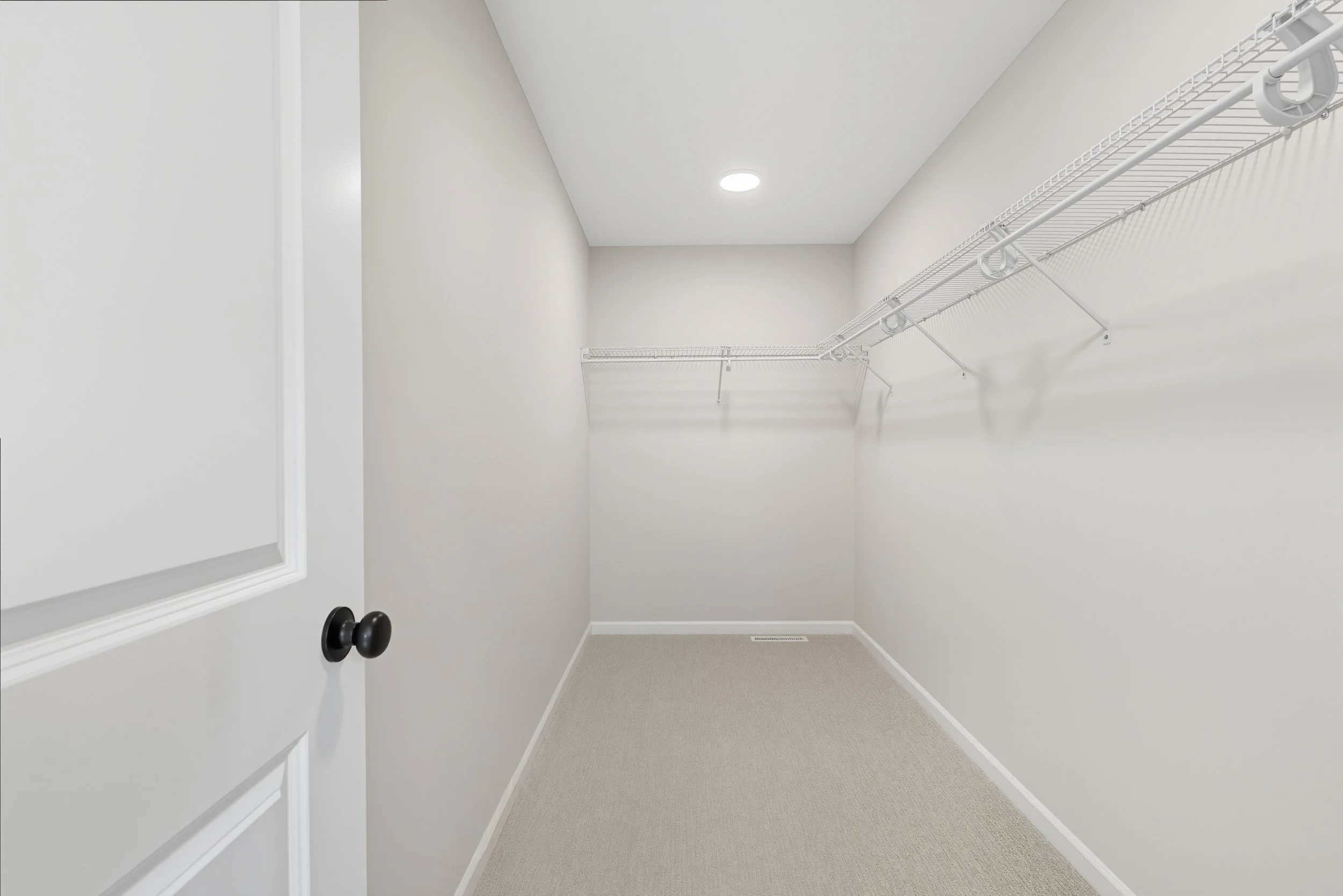 Empty walk-in closet with beige carpet, white walls, a white wire shelf, and ceiling light.