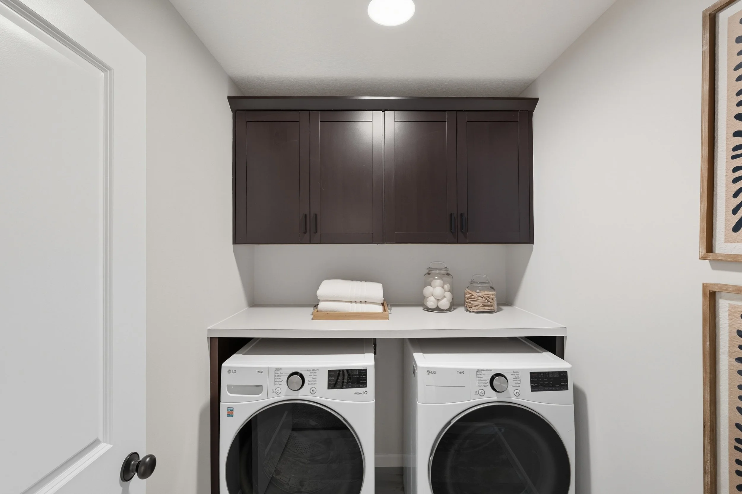 Laundry room with dark wooden cabinets, white washing machine, and dryer. Wall decor and laundry essentials on the countertop.