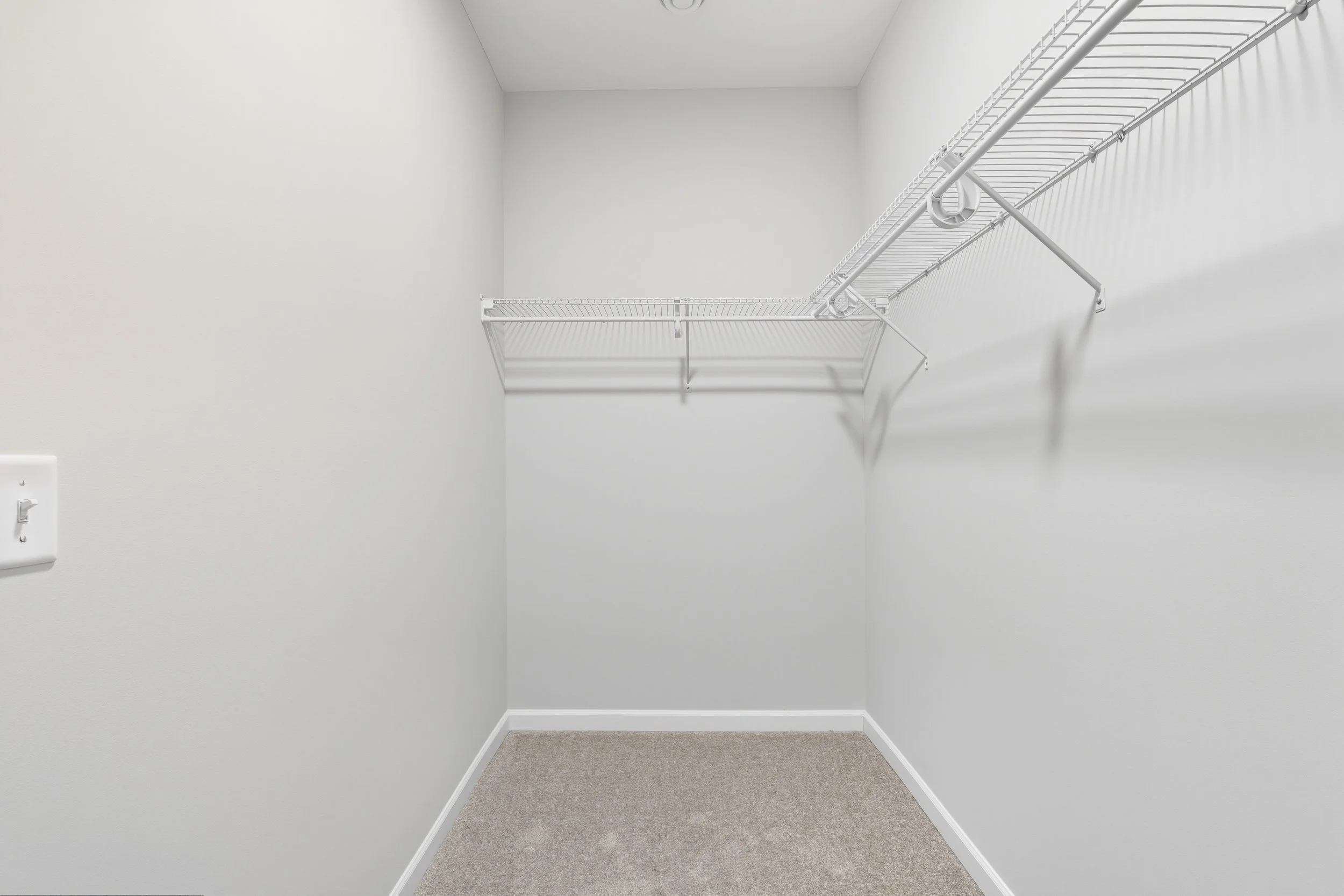 empty white walk-in closet with wire shelves and beige carpet flooring