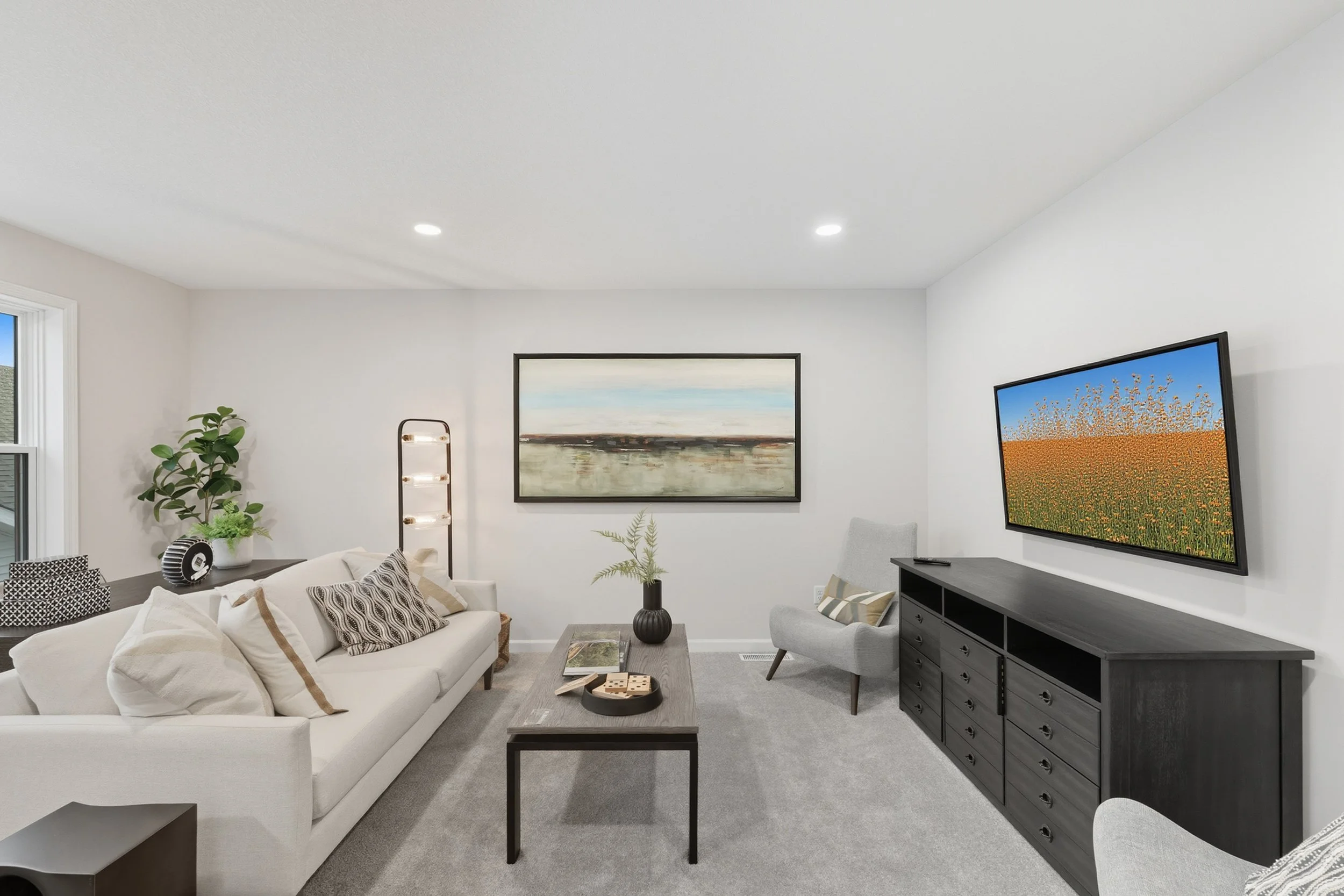 Modern living room with white sofa, gray chairs, art paintings, television, and decorative plants.