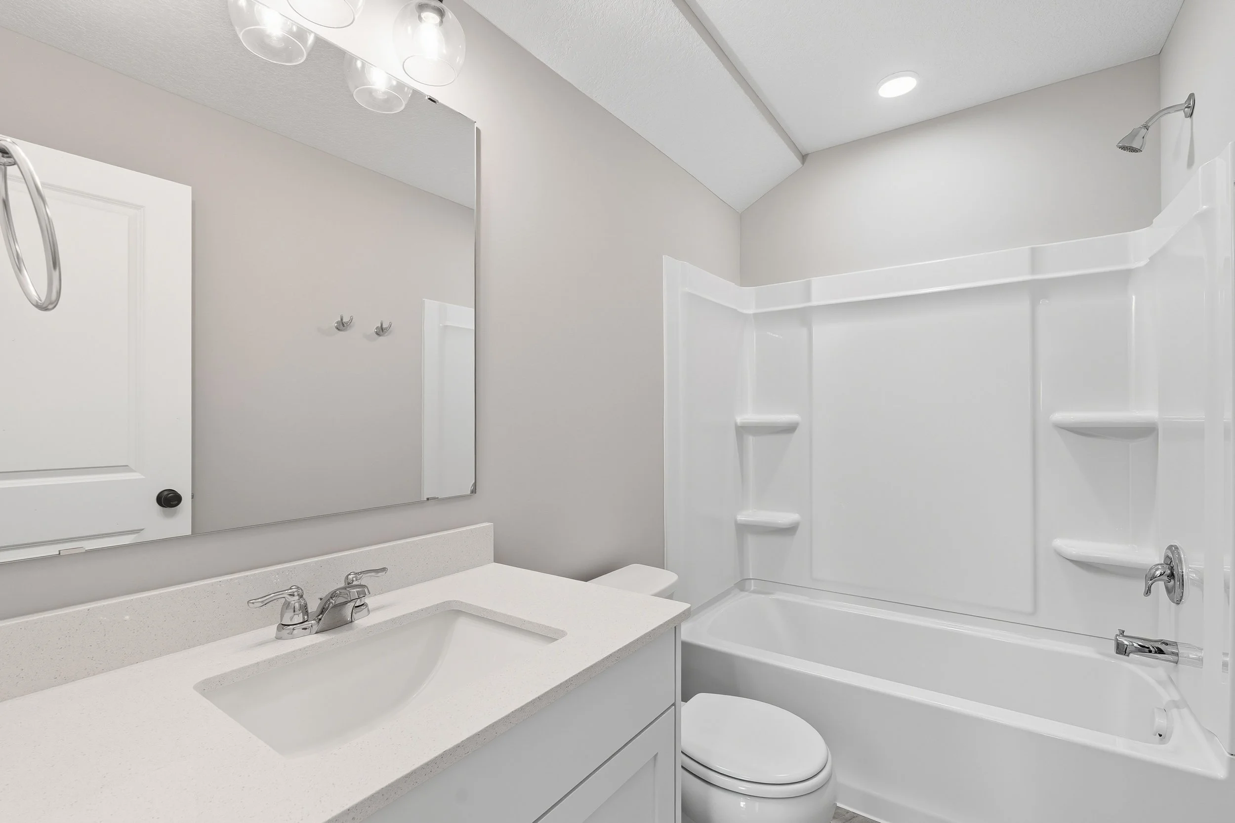 A clean bathroom with a white vanity, a mirror, a toilet, and a bathtub with a showerhead.