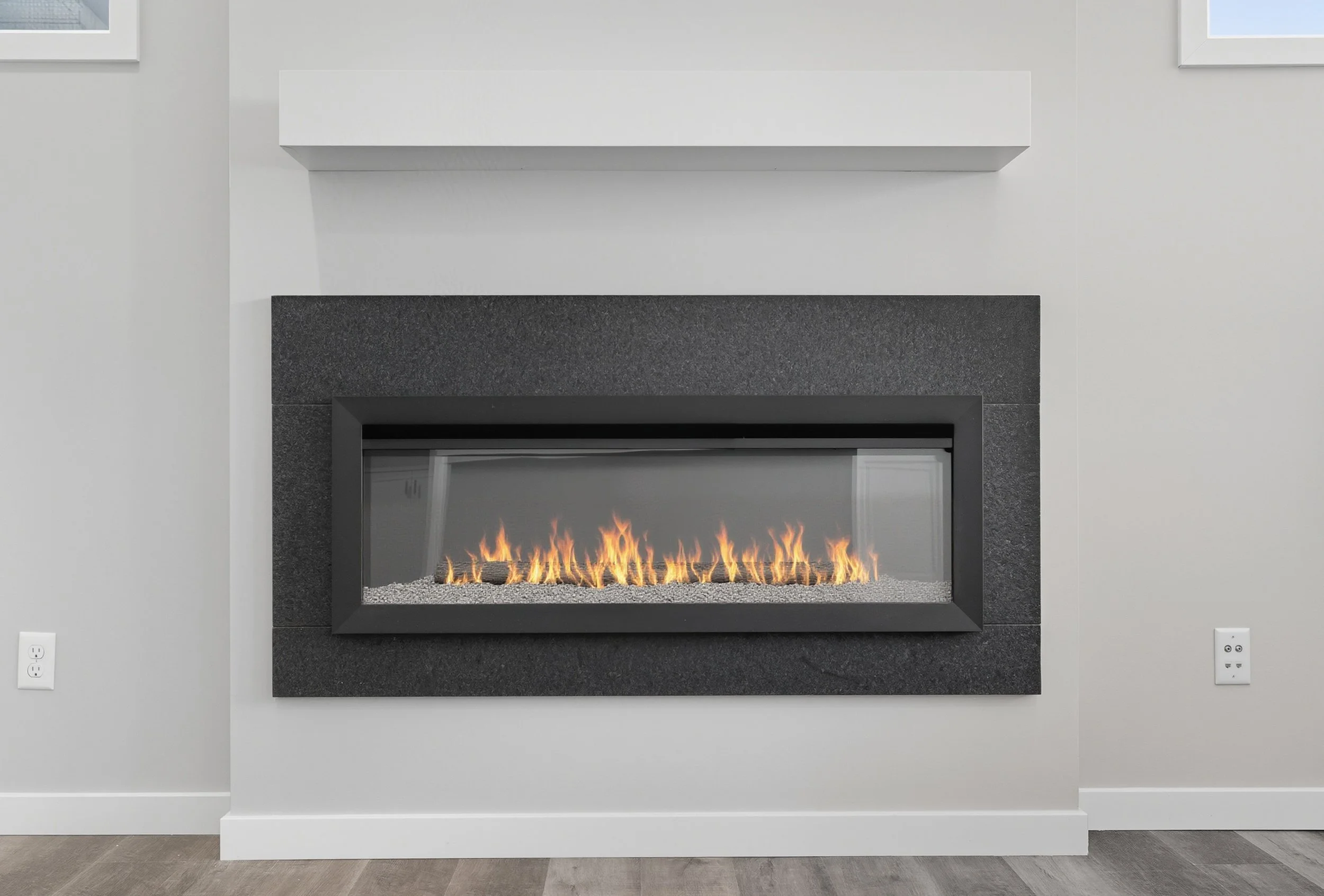 Modern fireplace with black frame and glass front, built into a light gray wall with white trim, electric flames, and gray stone surround, in a contemporary living space.
