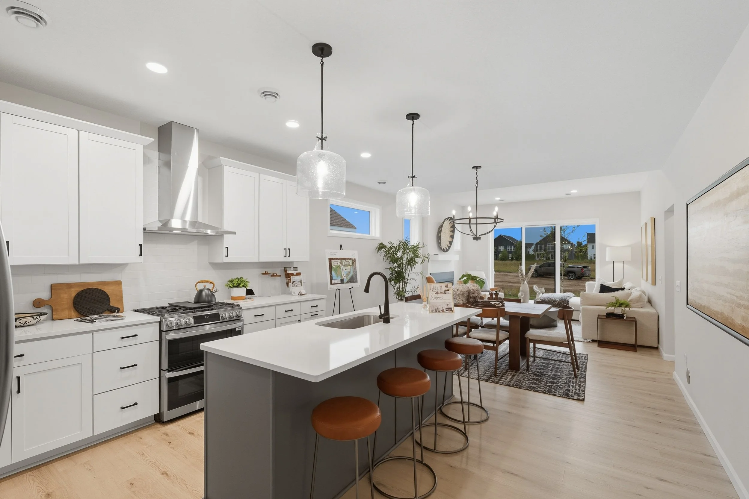 Open-concept kitchen and living room with white cabinetry, a kitchen island with brown stools, and a sitting area with a large window, sofa, and dining table.