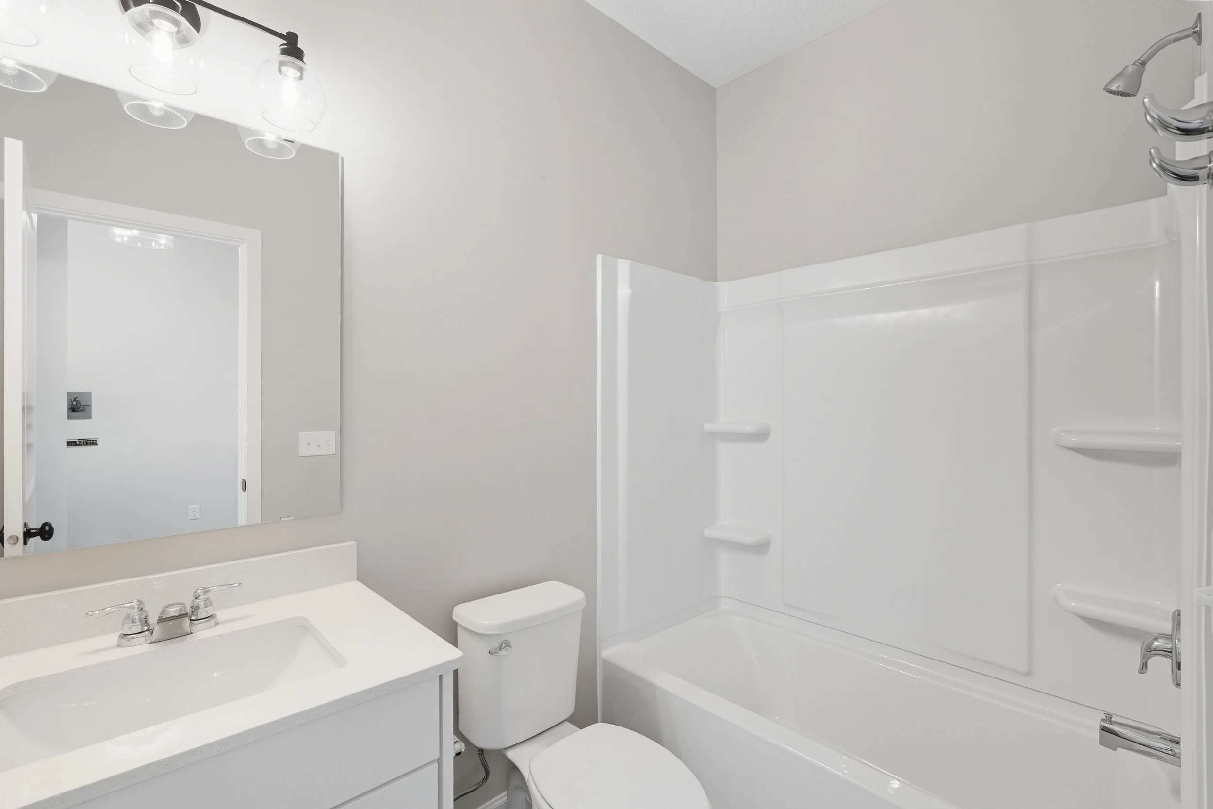 A white bathroom with a vanity, large mirror, toilet, and bathtub with a built-in shower.