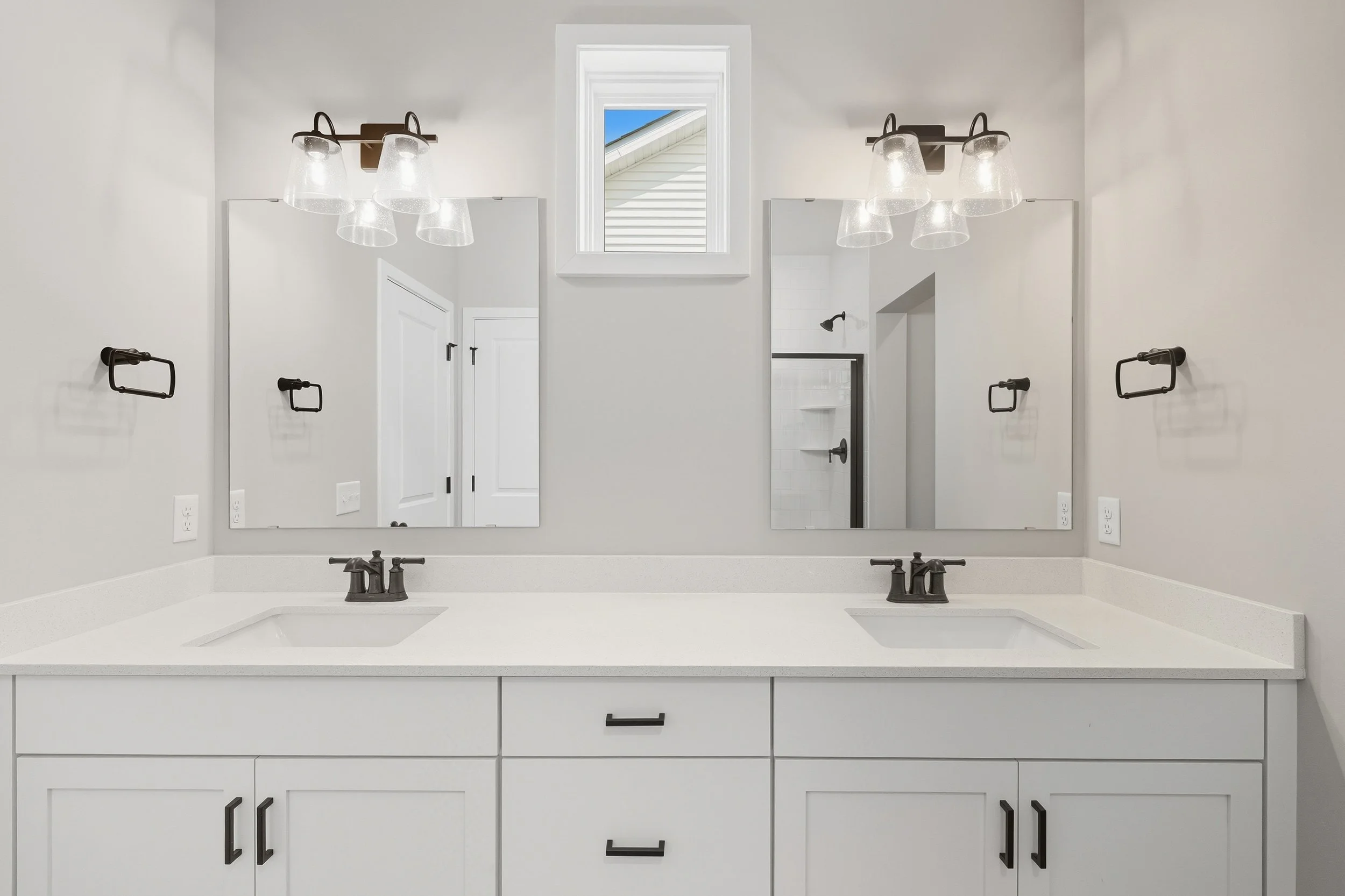Modern bathroom with double vanity, white cabinets, two mirrors, black fixtures, two wall lights, and a small window above the mirrors.