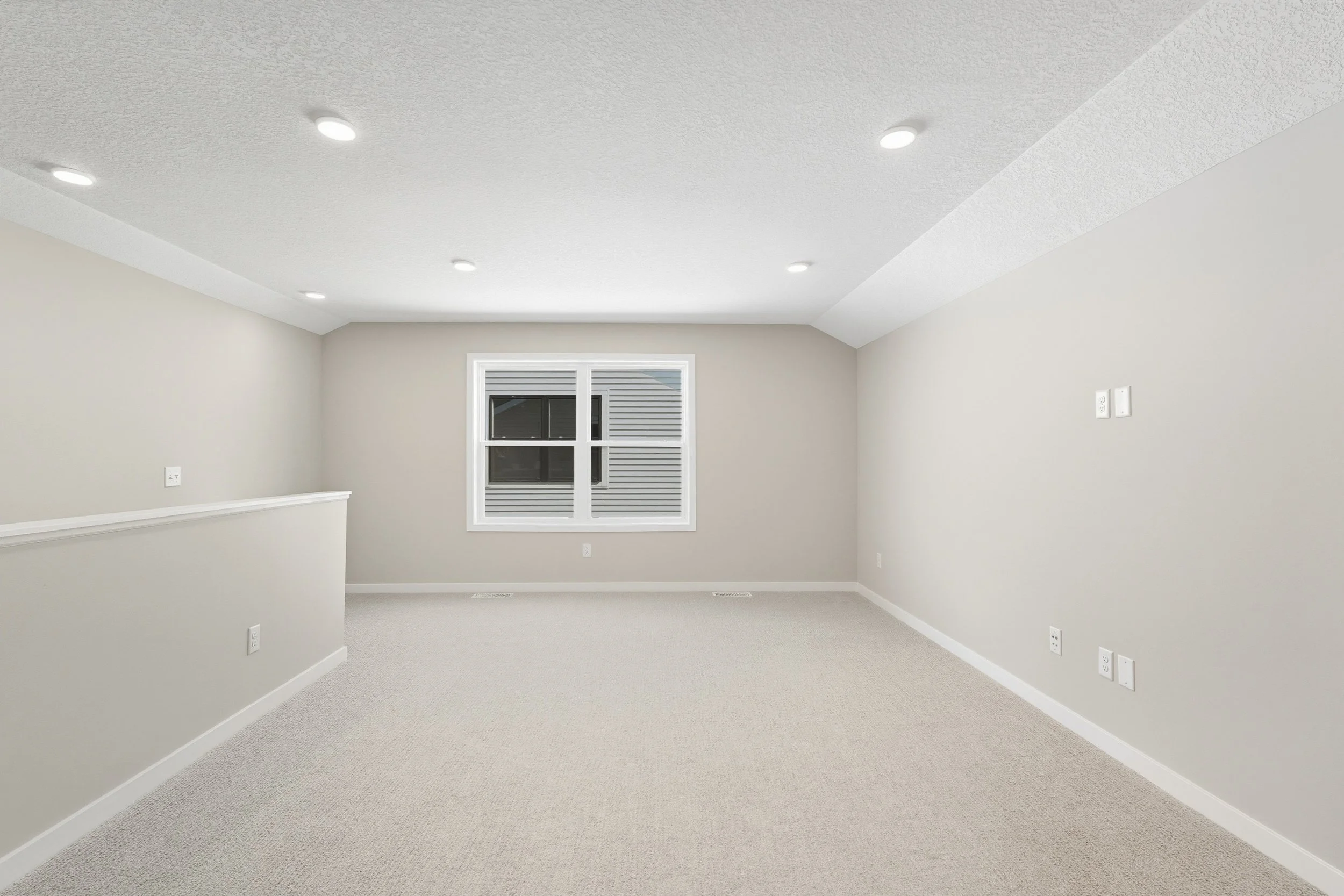 Empty, finished basement room with white walls, beige carpet, a window with blinds, and recessed ceiling lights.
