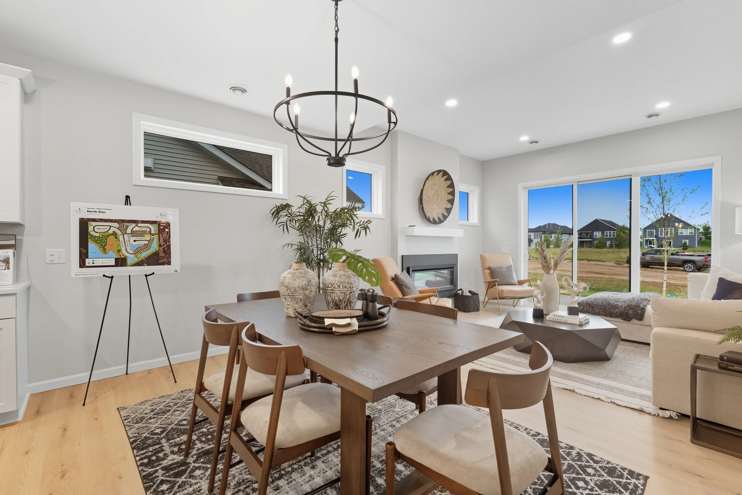 Open living and dining area with wood dining table, six chairs, beige sofa, armchairs, coffee table, large window, and modern fireplace.