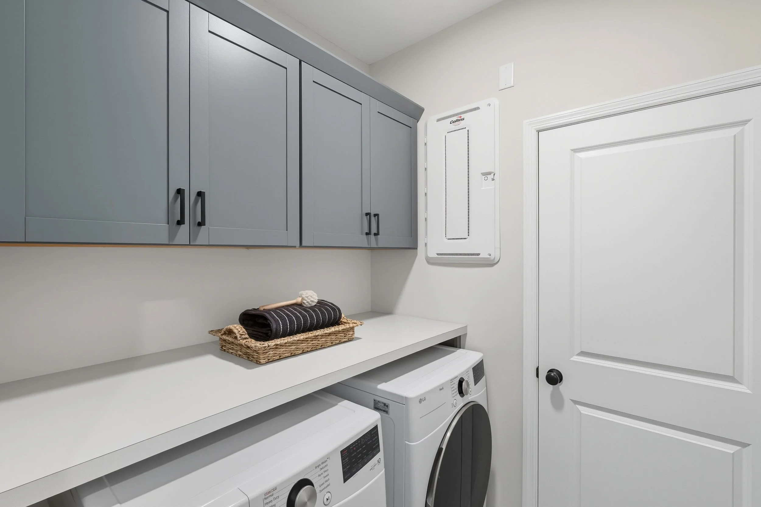 Laundry room with blue cabinets, white countertop, washer and dryer, basket with towels, and an electrical panel on the wall.