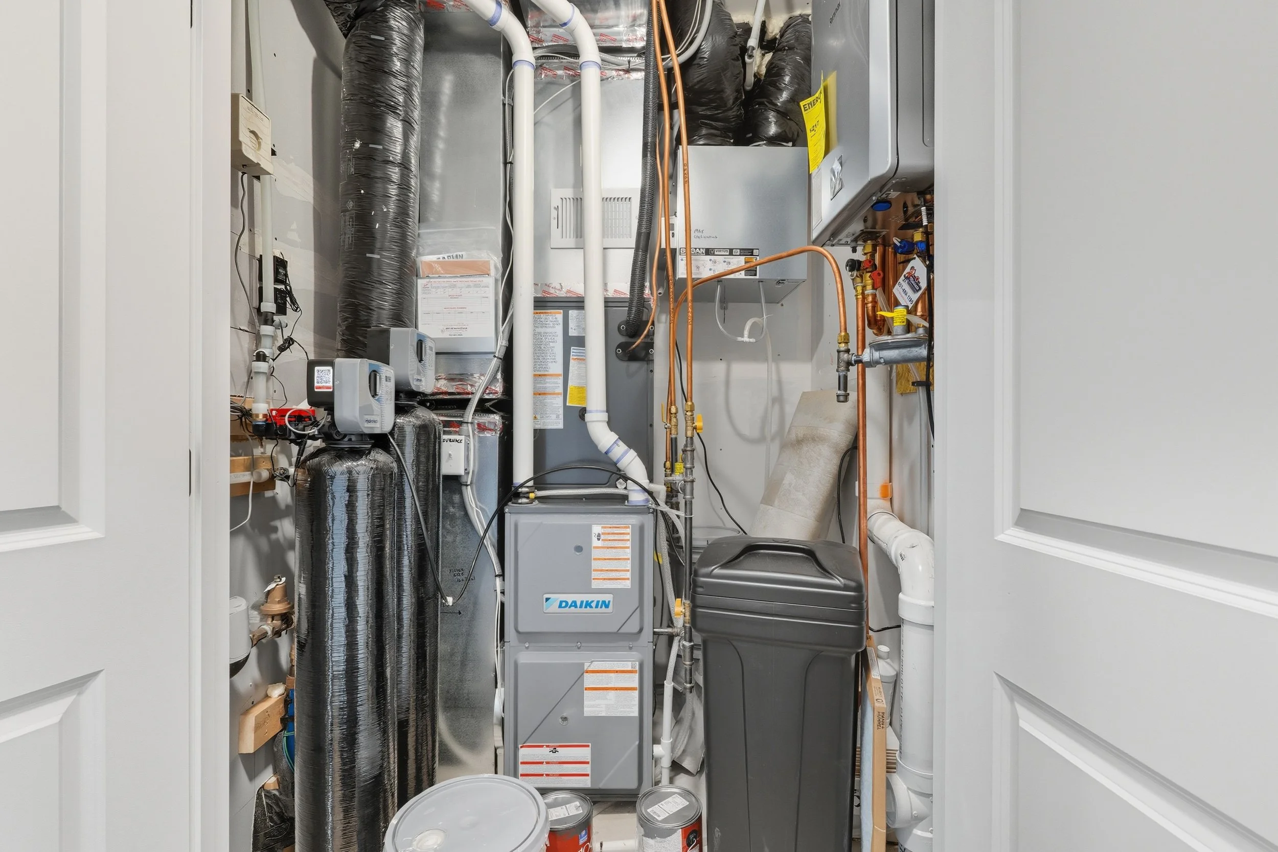A utility closet containing HVAC equipment, pipes, and electrical components.