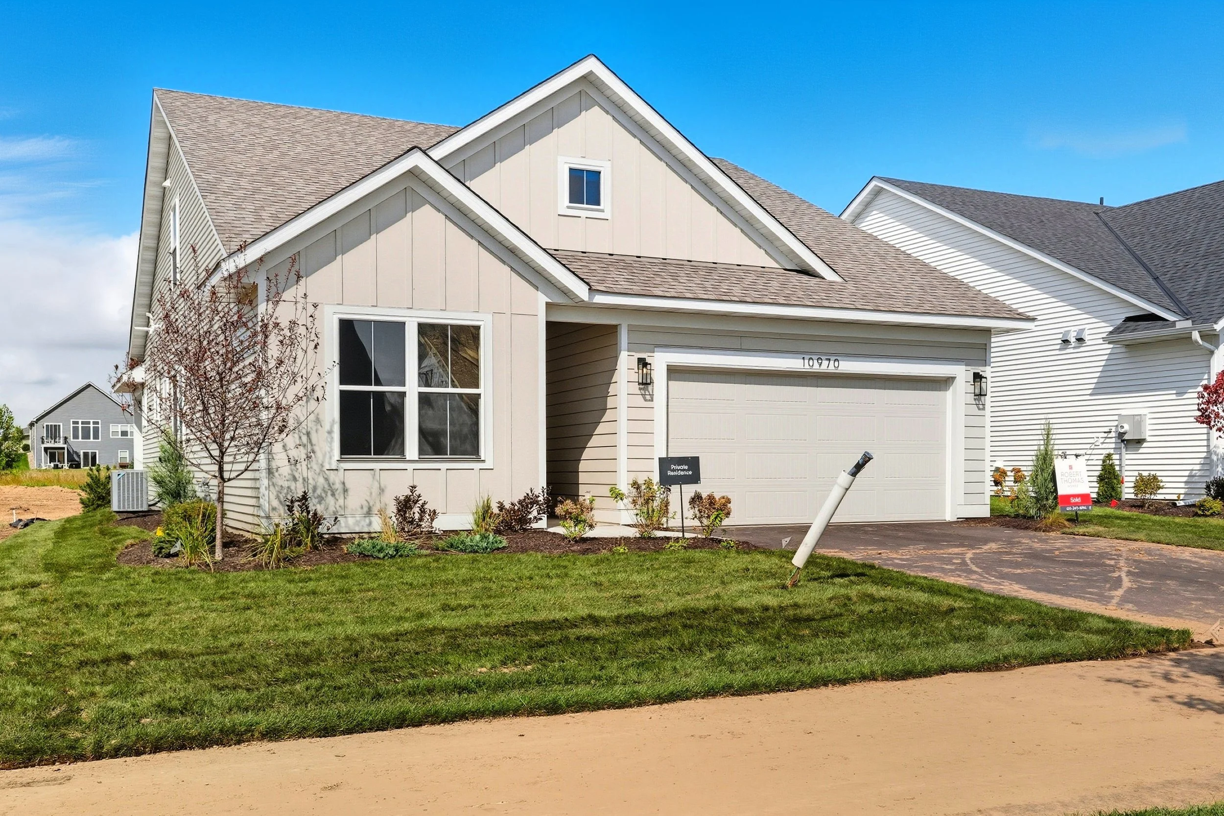 White suburban house with a two-car garage, landscaped yard, and clear blue sky.